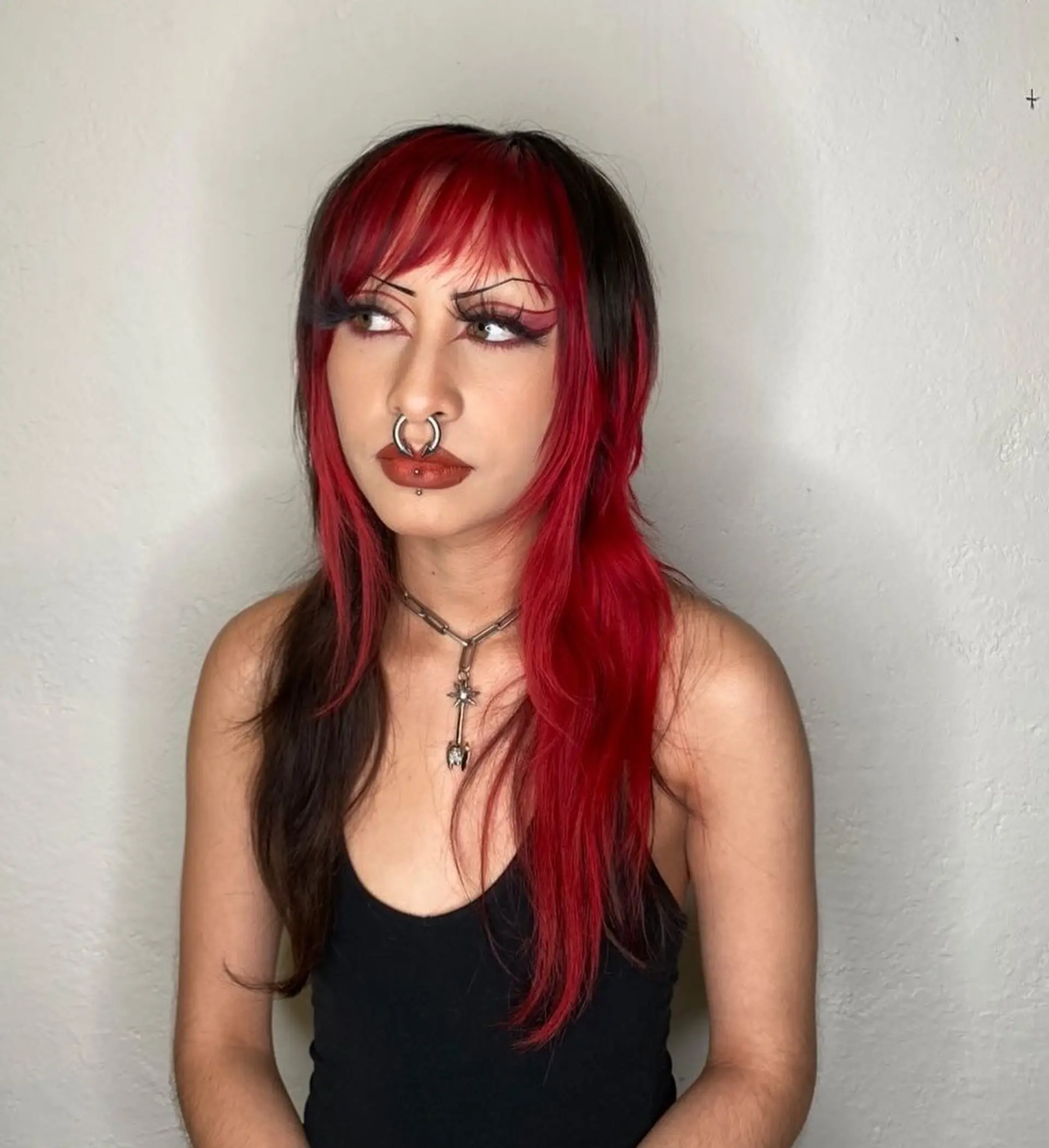 A layered alternative shag haircut featuring blunt front bangs, textured face-framing layers, and a vivid red and black color-blocked split dye. 1