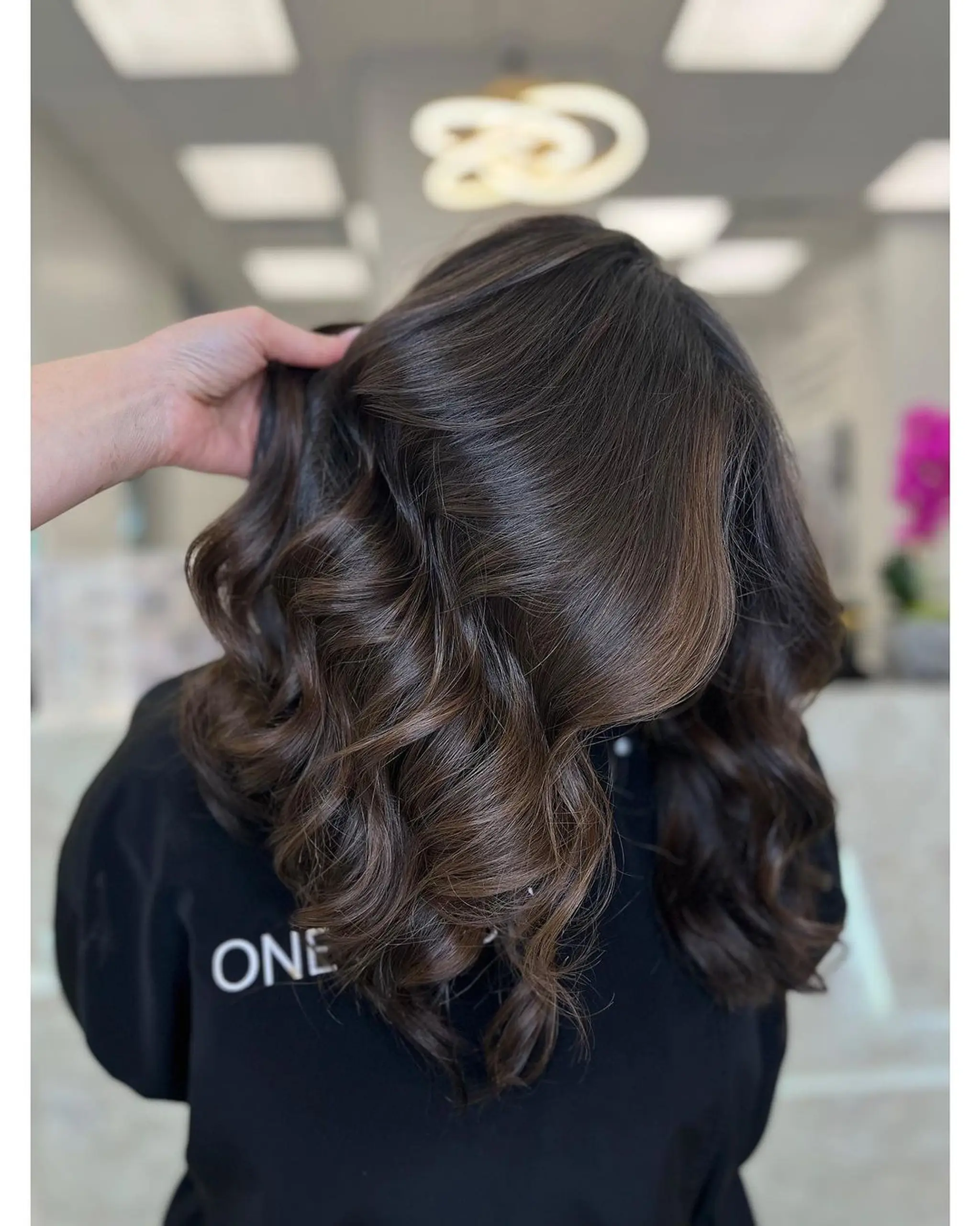 Medium-length dark brown hair styled into glossy, voluminous waves with soft, defined curls cascading beautifully to the ends.
