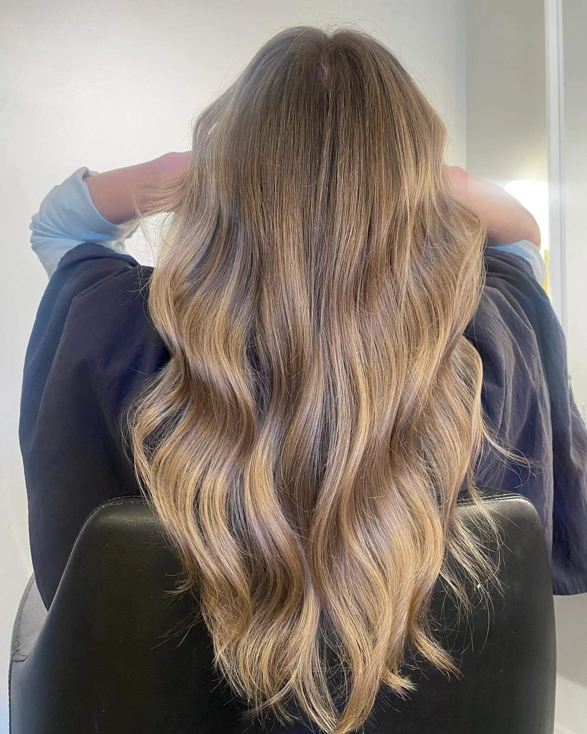 Long hair styled into loose, flowing soft waves featuring a blended dimensional balayage with warm honey and cool beige blonde highlights over a light brown base. 1