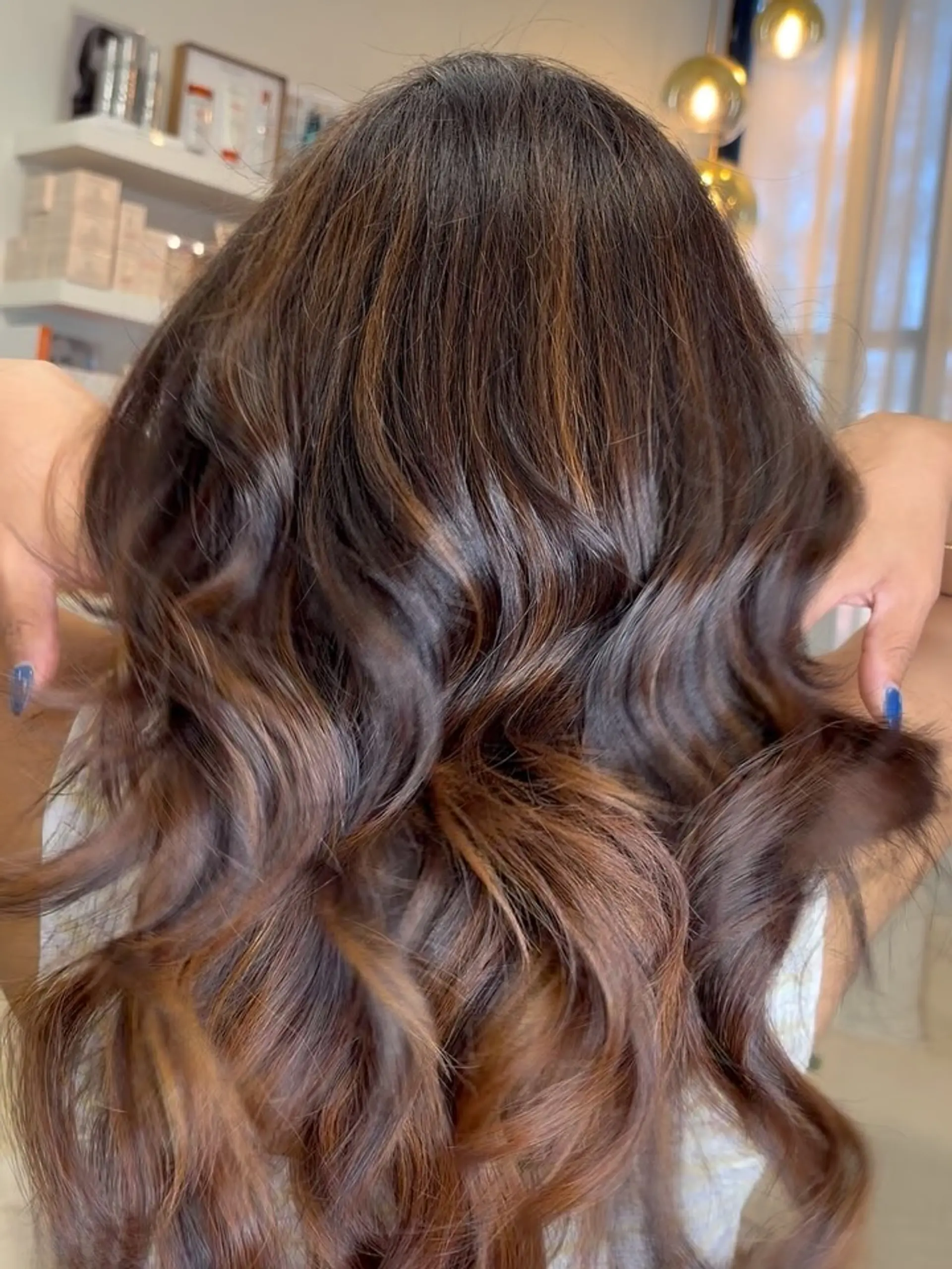 Long brunette hair styled in loose waves featuring blended warm caramel balayage highlights. 1