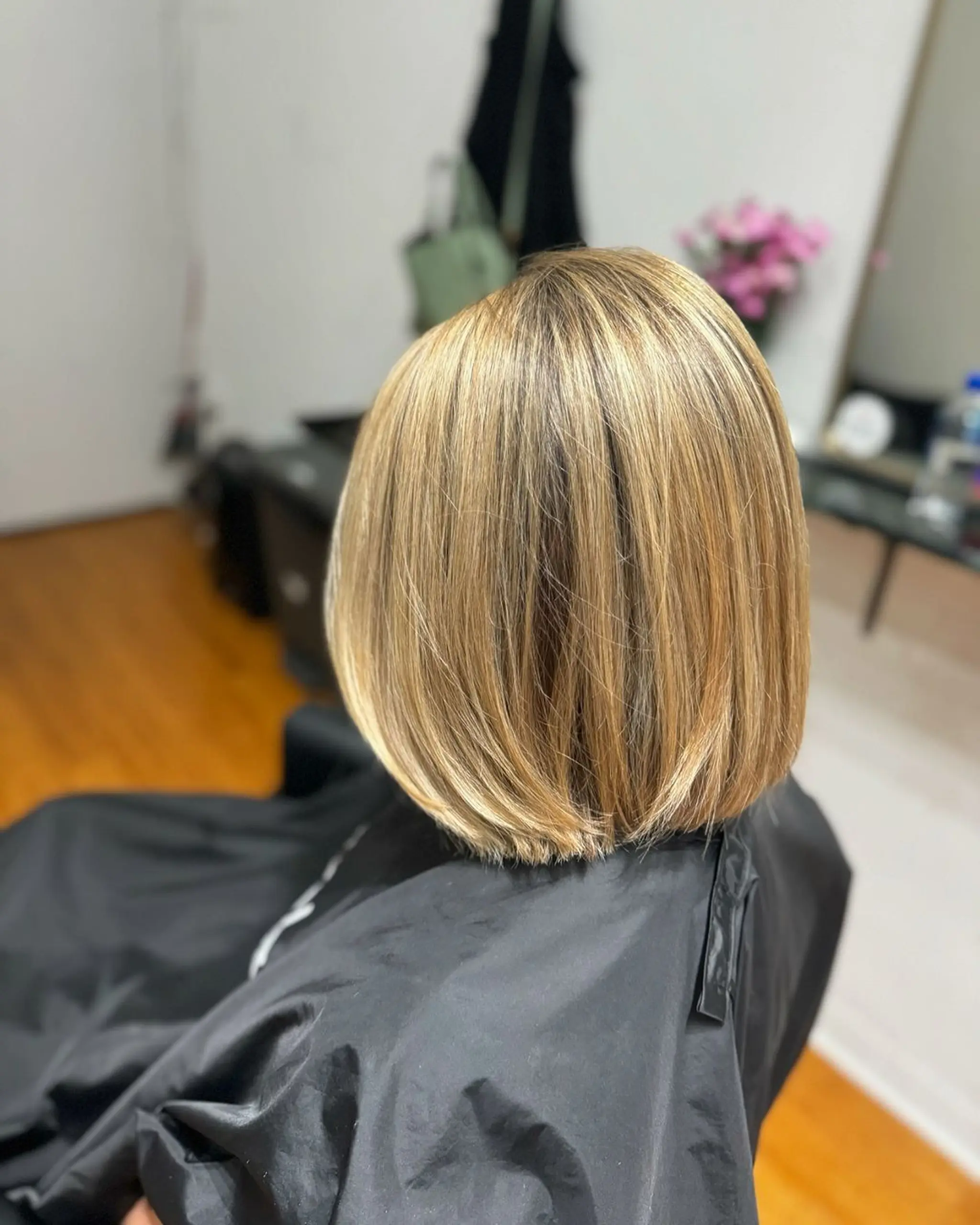 The hair is straight with a medium length, cut into a sleek bob. It features a blend of golden blonde and dark blonde colors. The style includes subtle layers for added volume and movement, resulting in a chic, polished look with a touch of glamour.