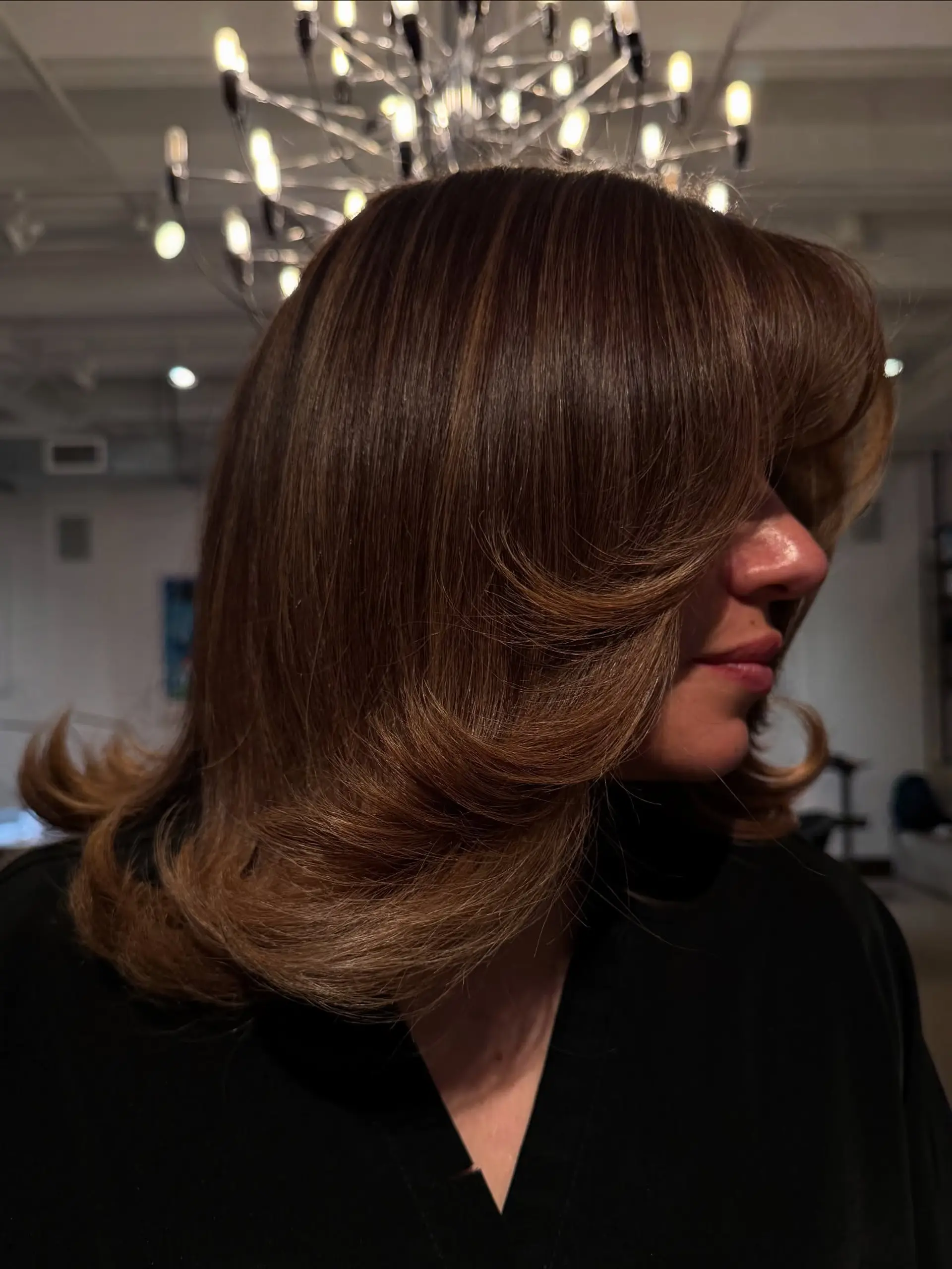 A medium-length layered cut styled into a bouncy blowout with exaggerated flipped ends, face-framing sweeping fringe, and dimensional caramel highlights. 1