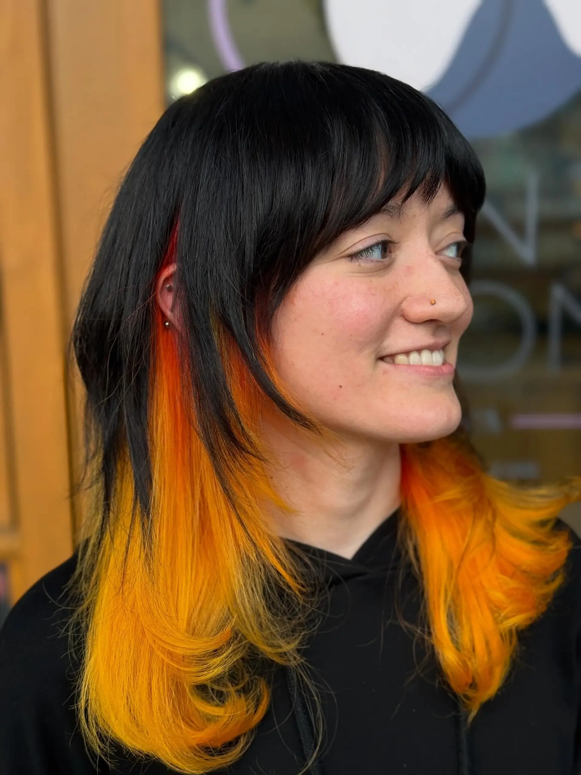 Medium-length shag cut with full textured bangs, featuring a sleek jet black top canopy contrasting sharply against bright fire orange and yellow underlights underneath. 1