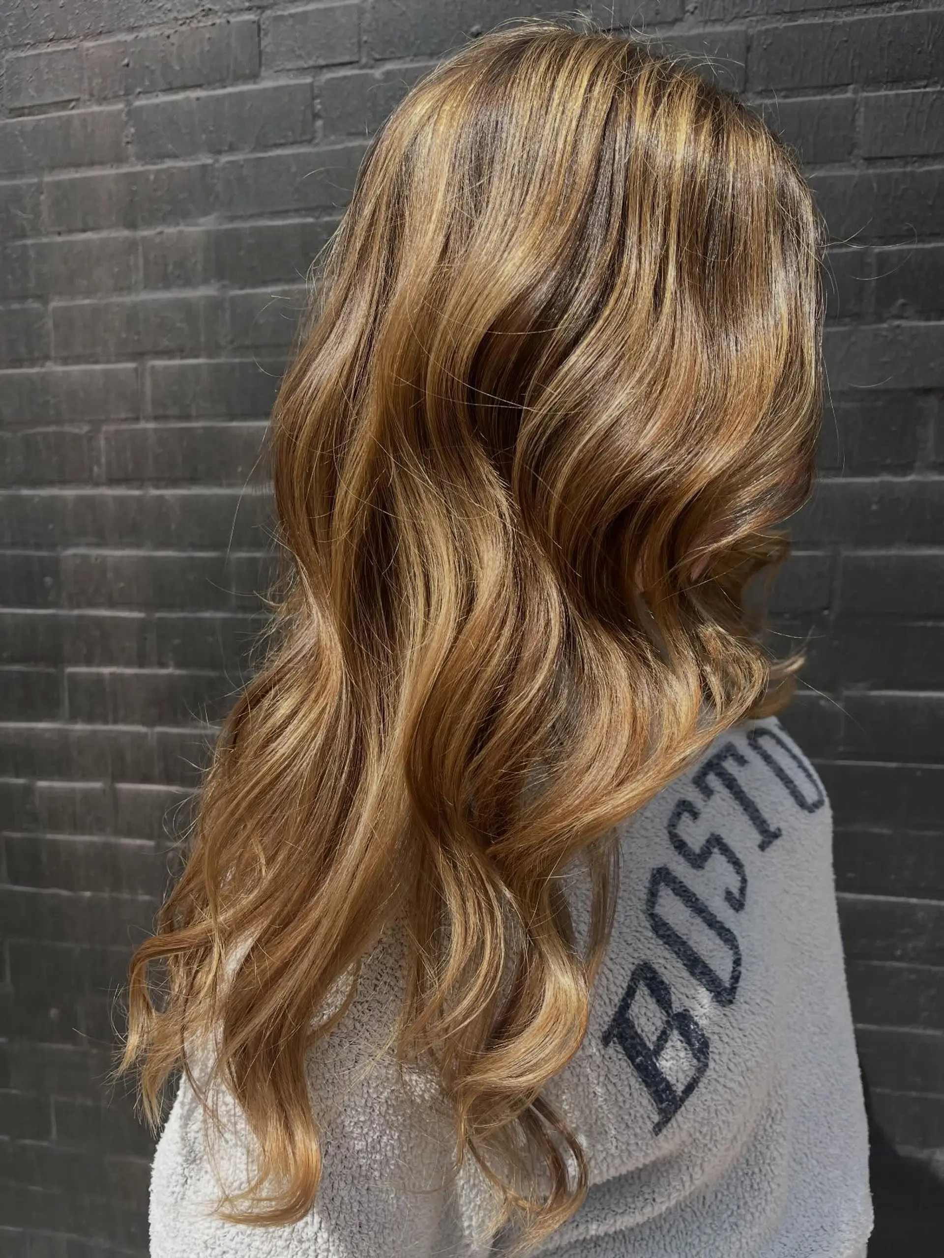 Long dimensional caramel and golden blonde highlights styled in loose, glossy waves. 1