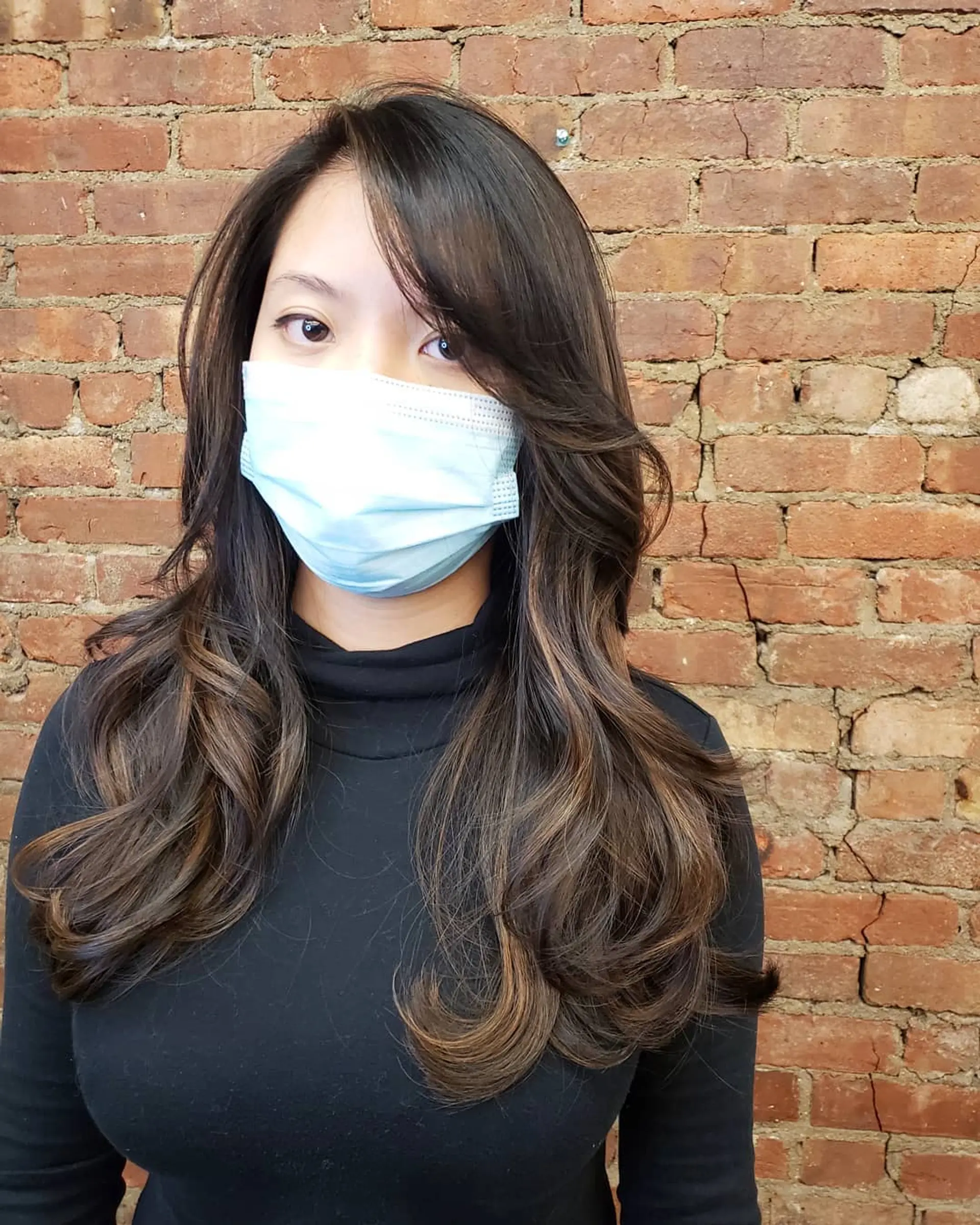 Long layered brunette hair with subtle warm balayage highlights, styled into soft outward curls with side-swept fringe. 1