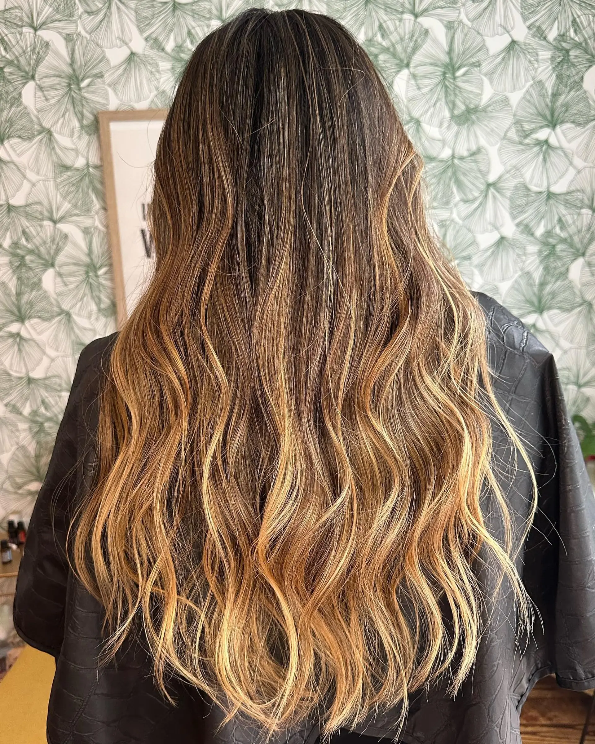 Long dark hair enhanced with warm caramel and golden highlights, styled into soft loose waves. 1
