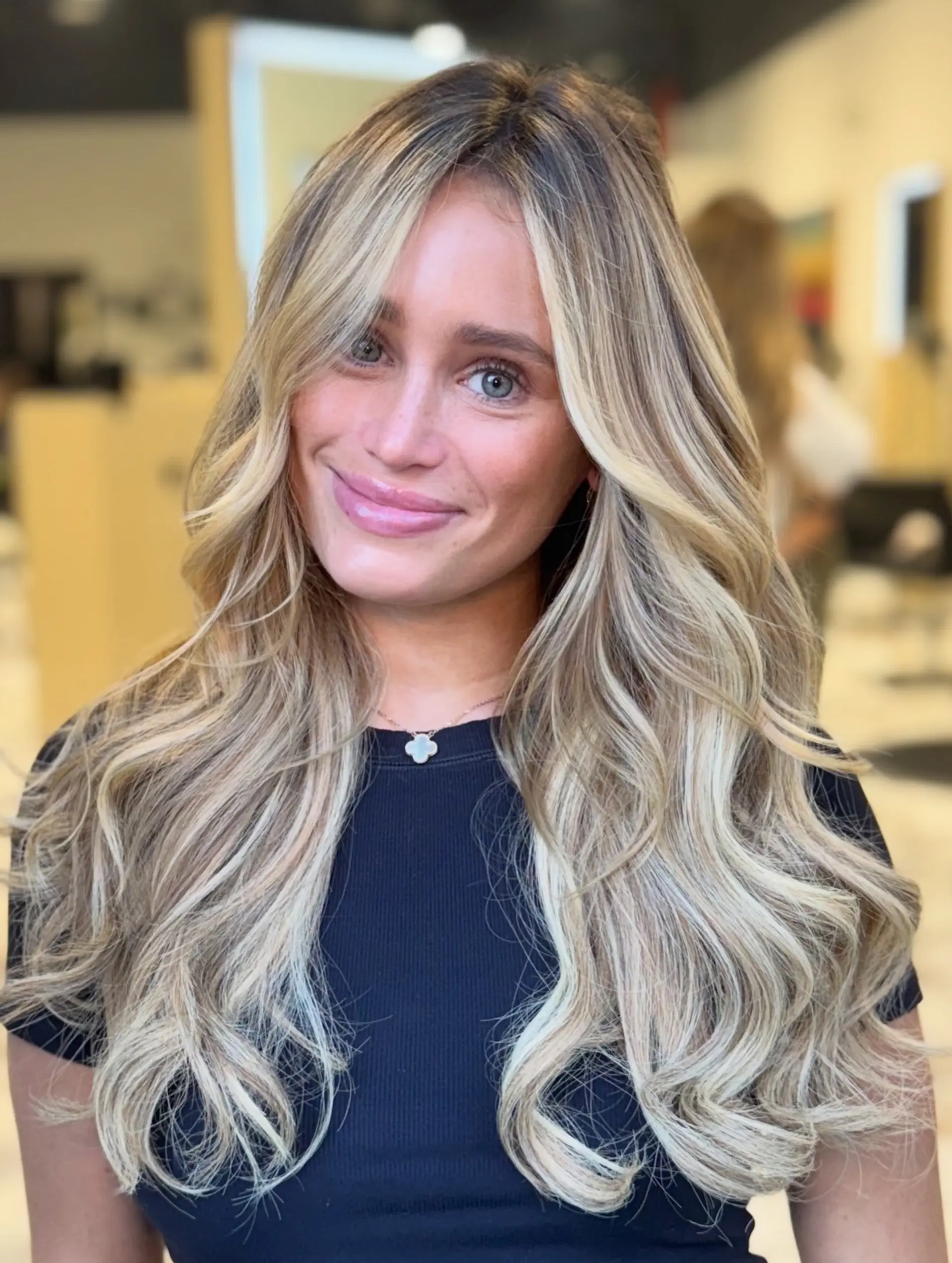 Voluminous long blonde hair styled with soft, cascading waves and face-framing curtain bangs. 1