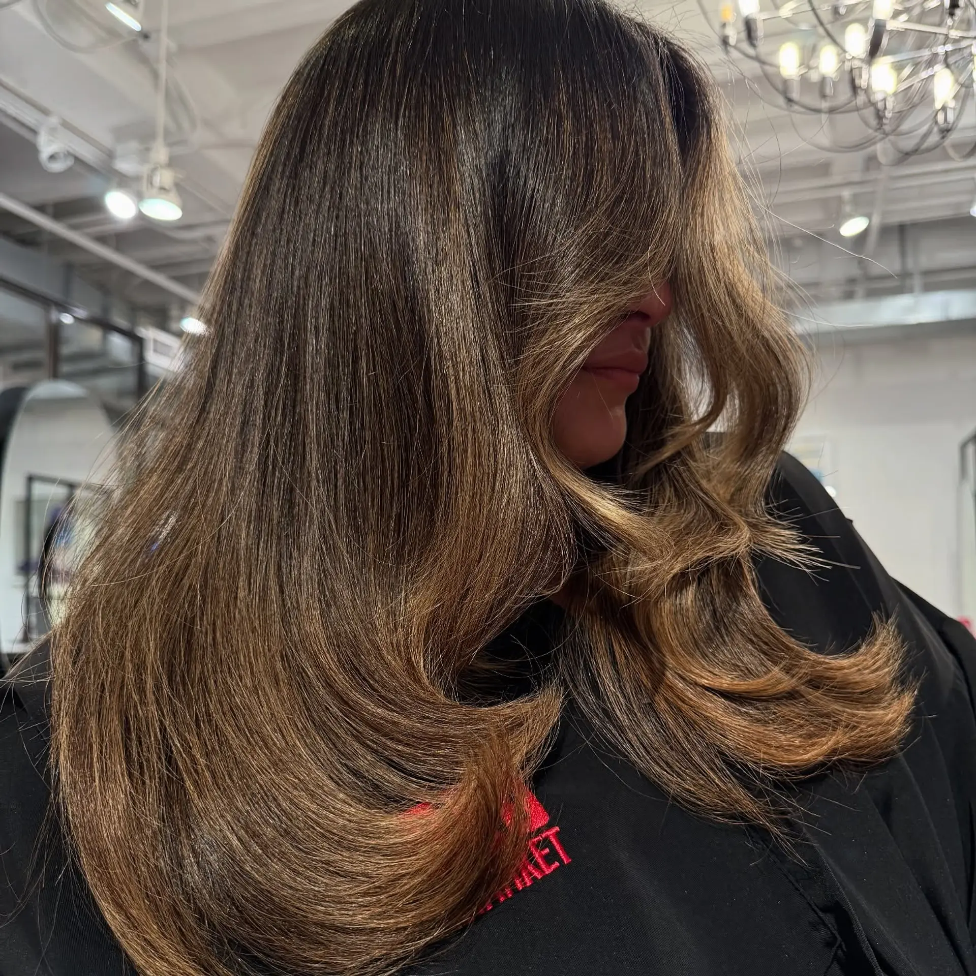 Long layered brunette hair with seamless caramel balayage highlights, styled in a polished, voluminous blowout with soft inward curled ends. 1