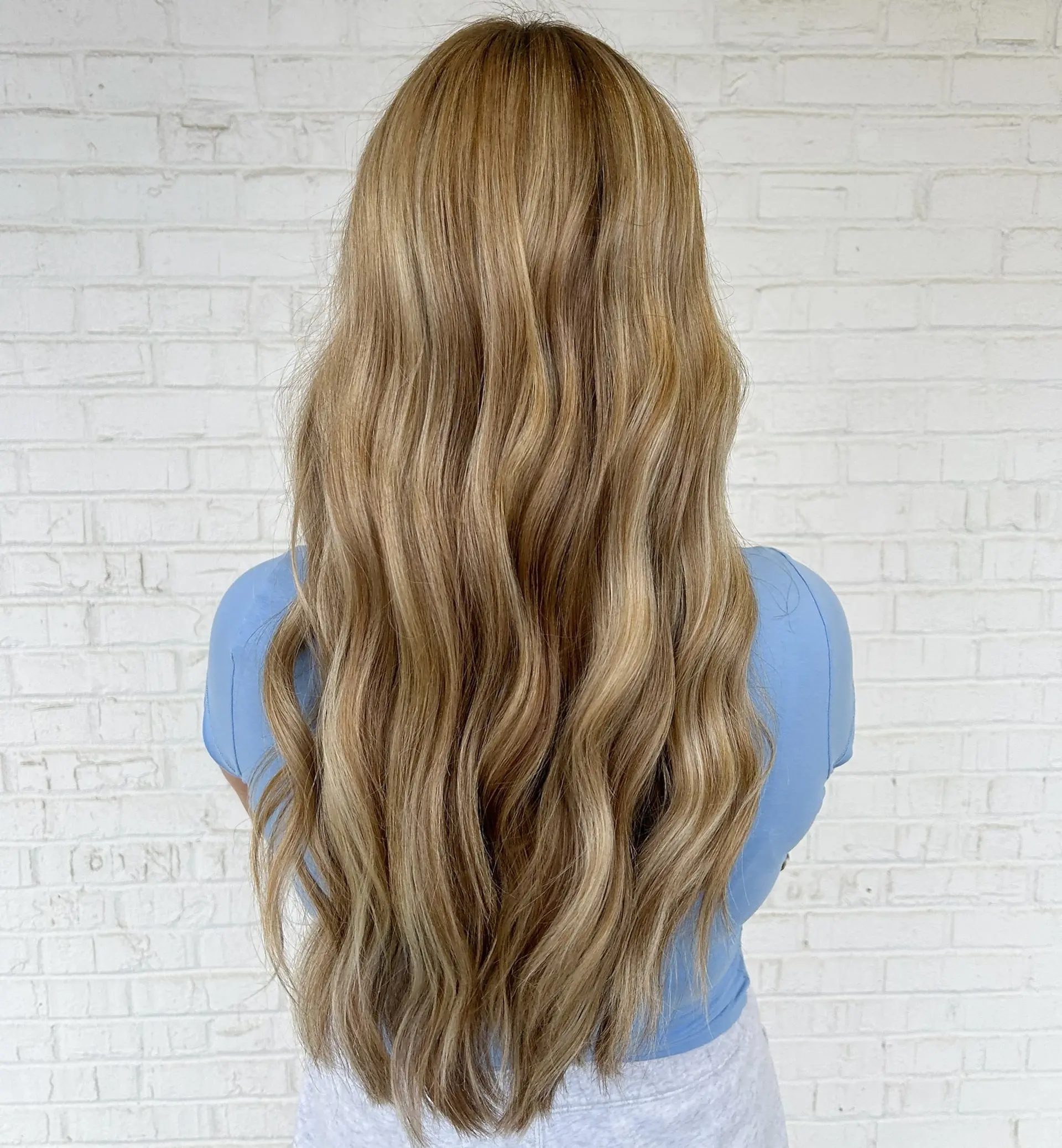 Long honey blonde hair featuring seamless dimensional highlights styled into soft, cascading waves. 1