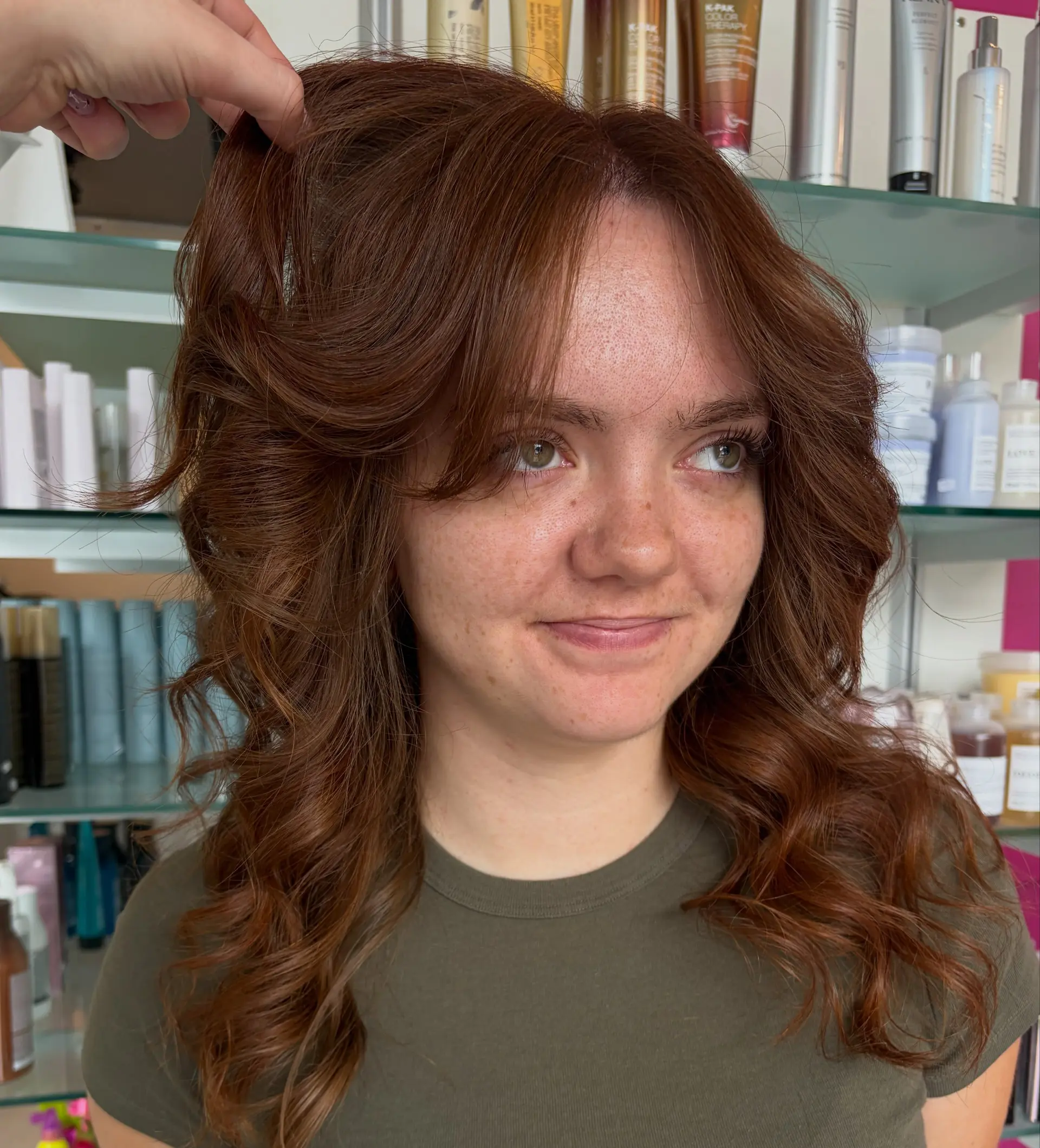 Medium-length layered cut styled with voluminous, bouncy curls and soft curtain bangs in a rich auburn hue. 1