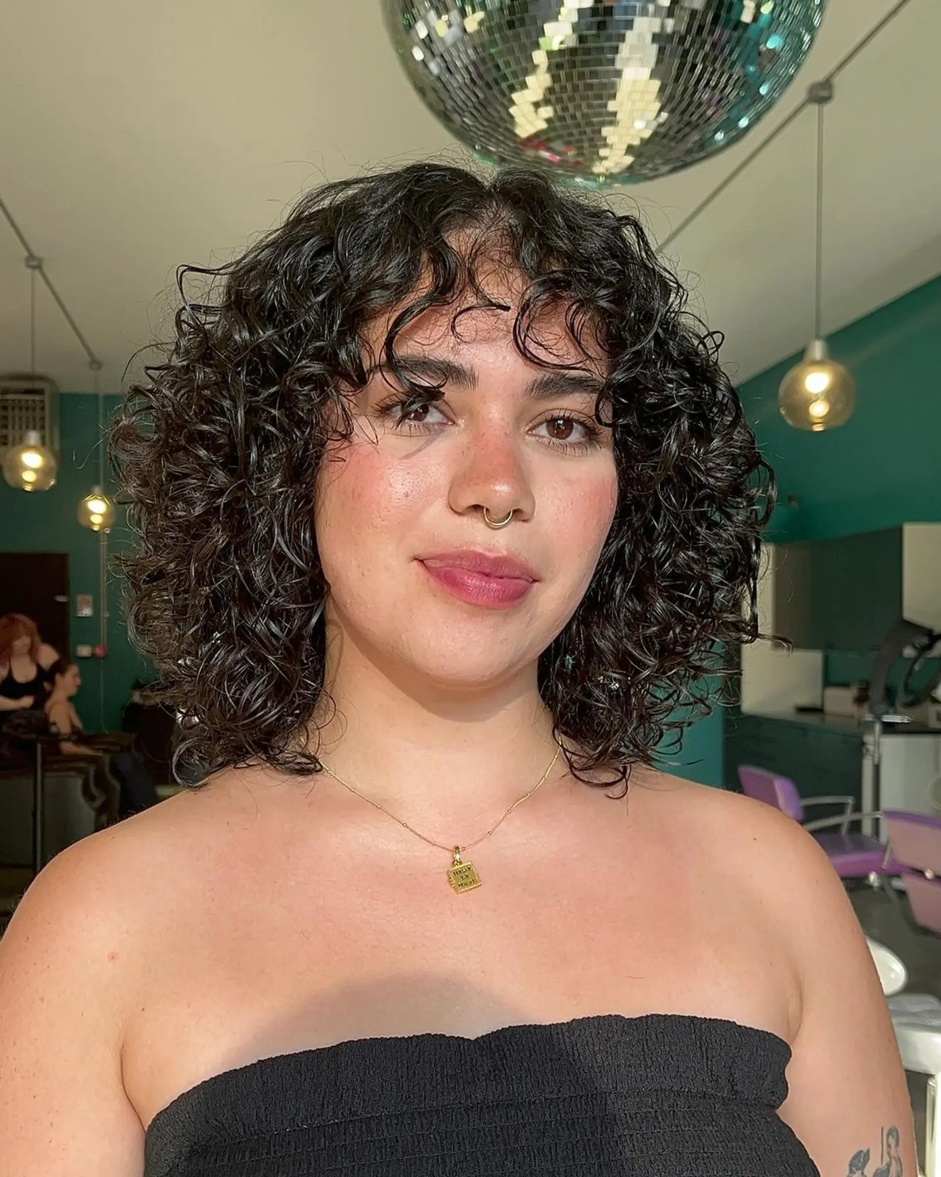 Medium-length curly hairstyle with voluminous curls and a soft fringe, featuring a lustrous natural shine and balanced layers. 1