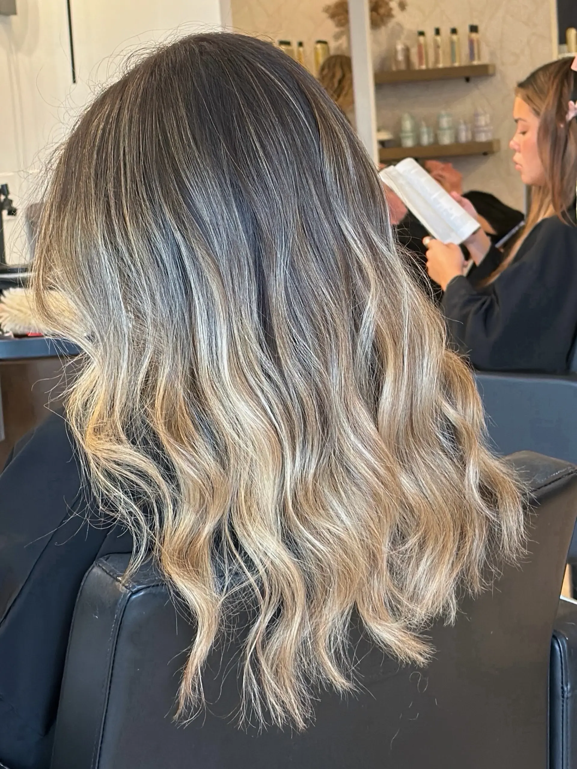 Long dark-rooted hair blended into cool blonde dimensional highlights, finished in soft flowing waves. 1