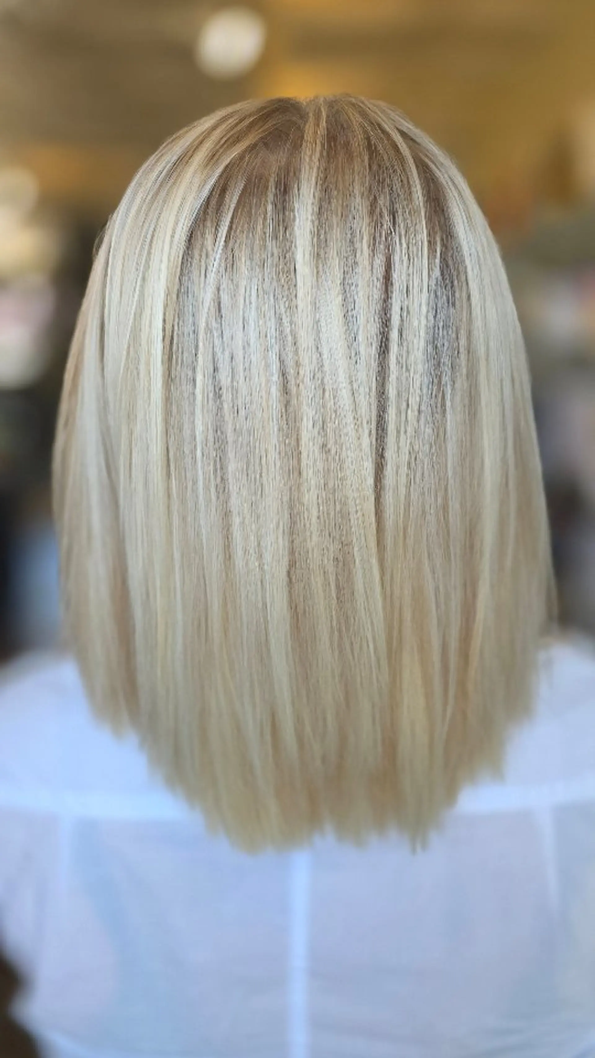 A medium-length straight blonde lob cut with subtle texture and seamless, dimensional highlights that add fullness. 1
