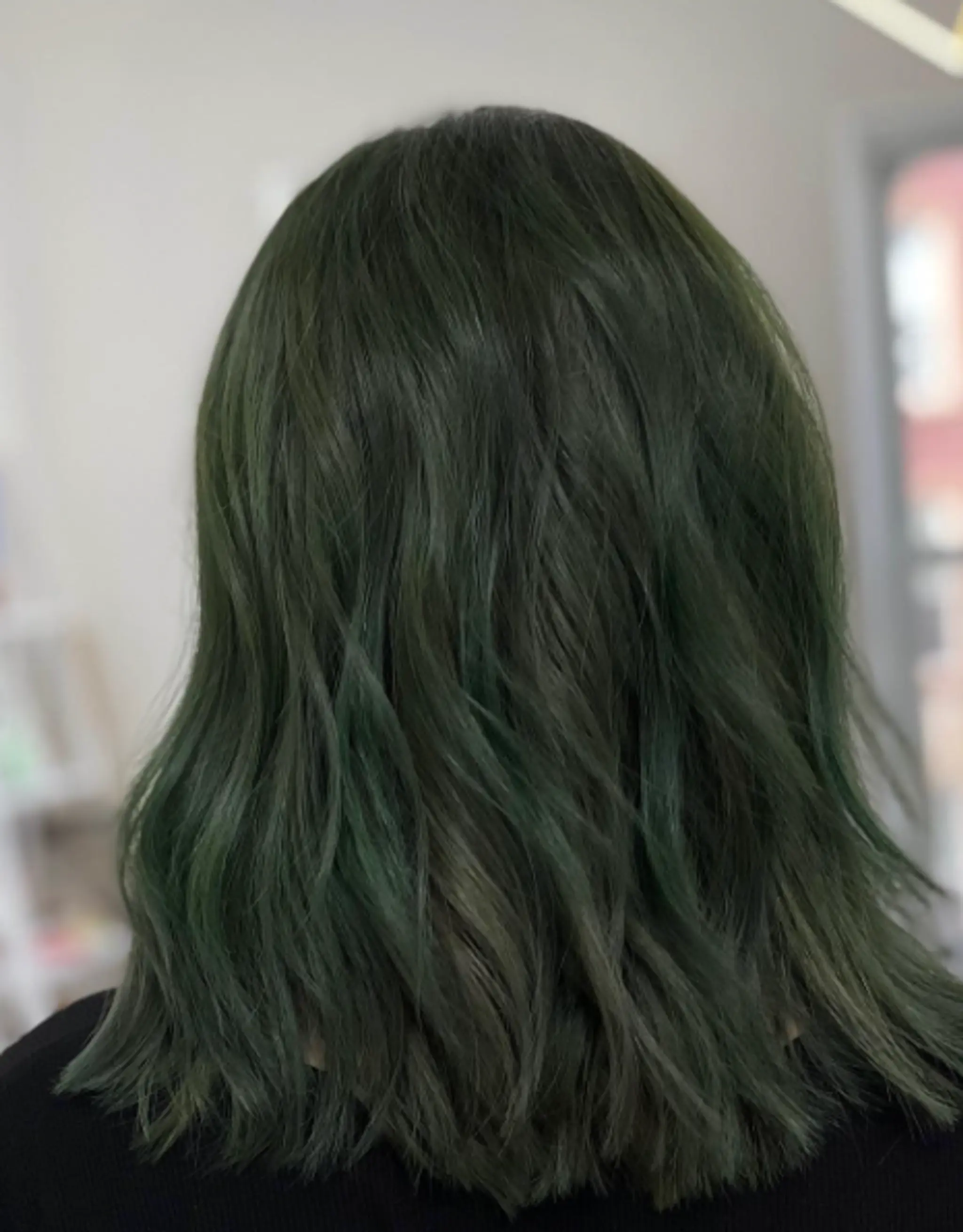 Medium-length wavy hair with natural layers and dyed a deep green, creating a forest-like, ethereal look.