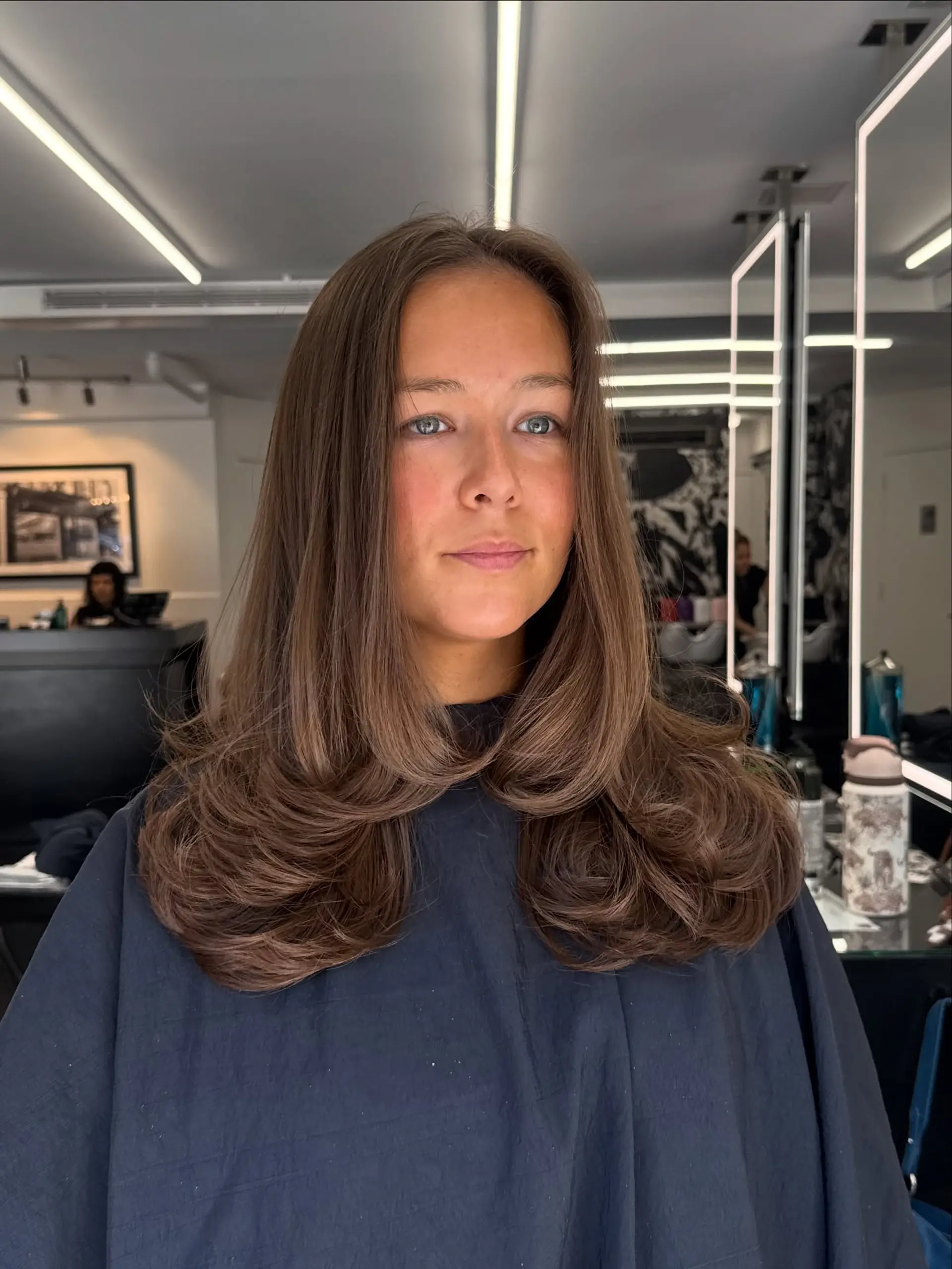 Long medium-brown hair styled in a voluminous blowout with face-framing layers curled inward at the ends. 1