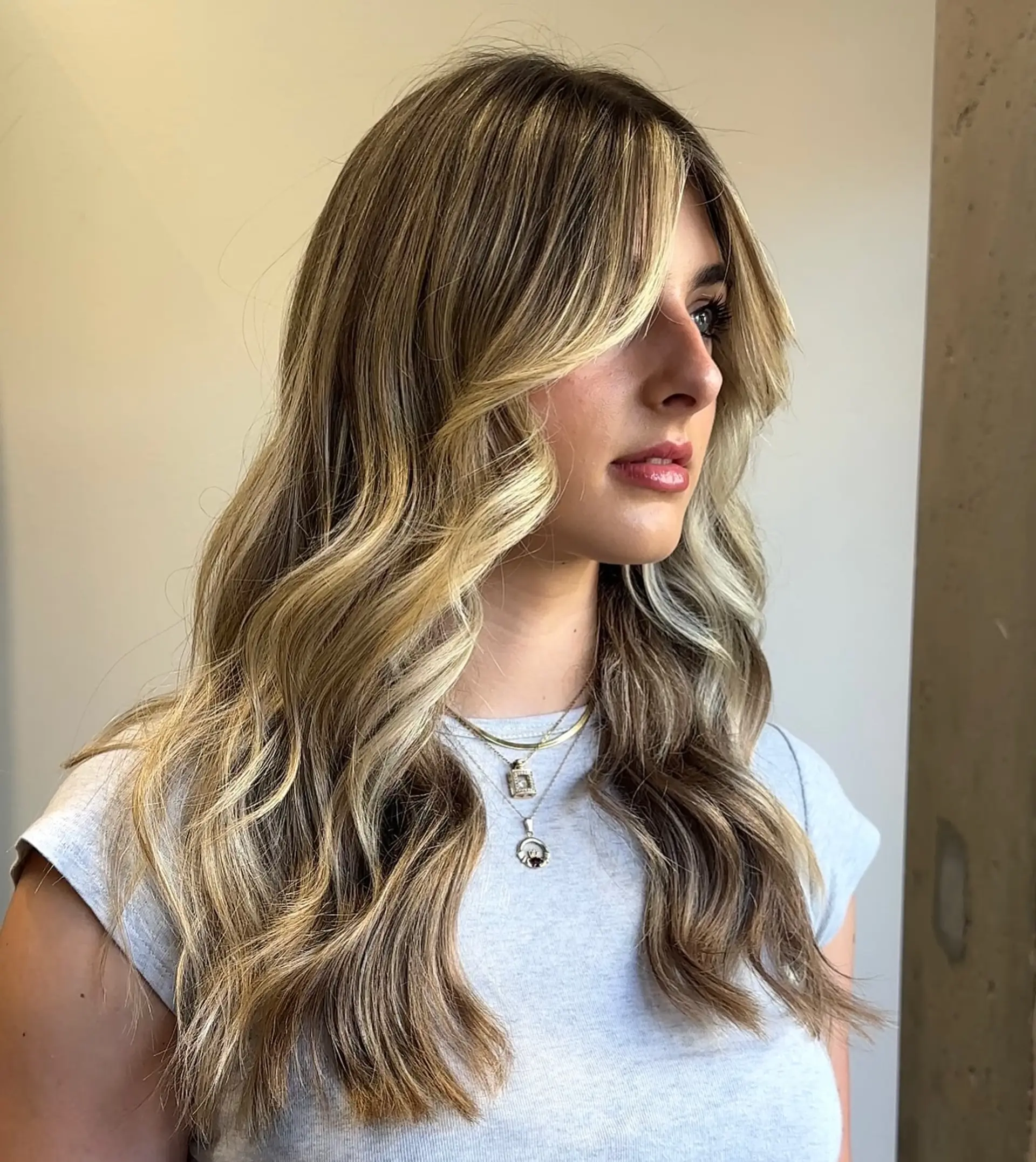 Long, wavy hairstyle featuring a bronde balayage, curtain bangs, and face-framing layers. 1