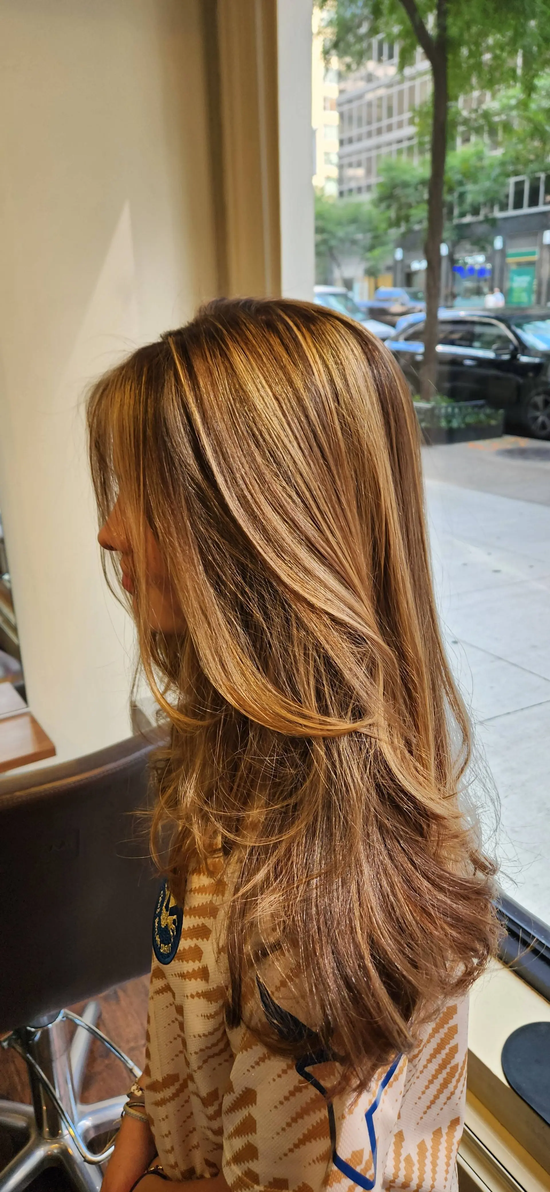 Long hair featuring warm golden-blonde highlights throughout, cut with cascading face-framing layers and styled with a smooth, voluminous blowout. 1