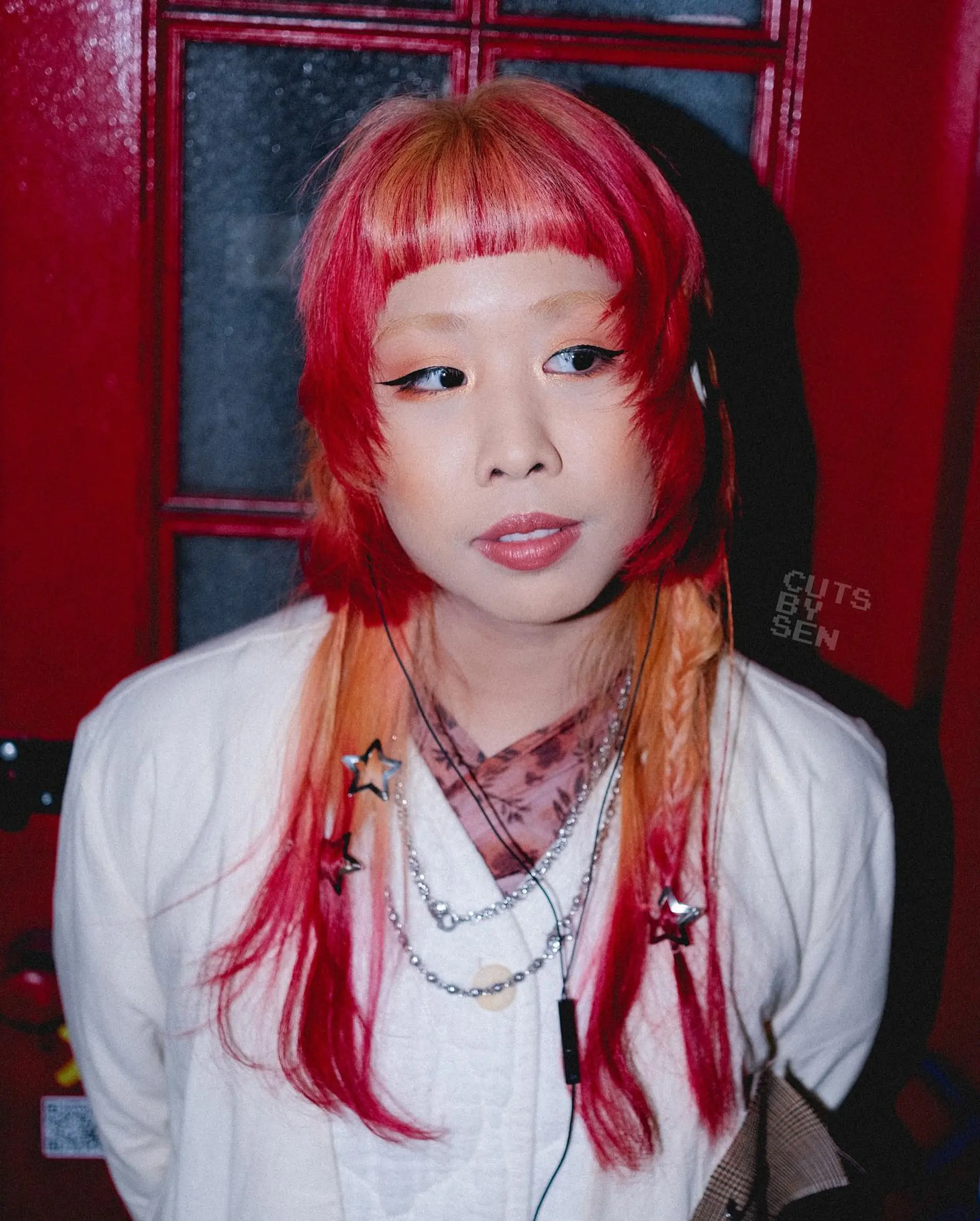 A modern, textured hime cut featuring blunt micro bangs, sculpted crimson face-framing layers, and long peachy-orange lengths styled with delicate braids and star clips. 1
