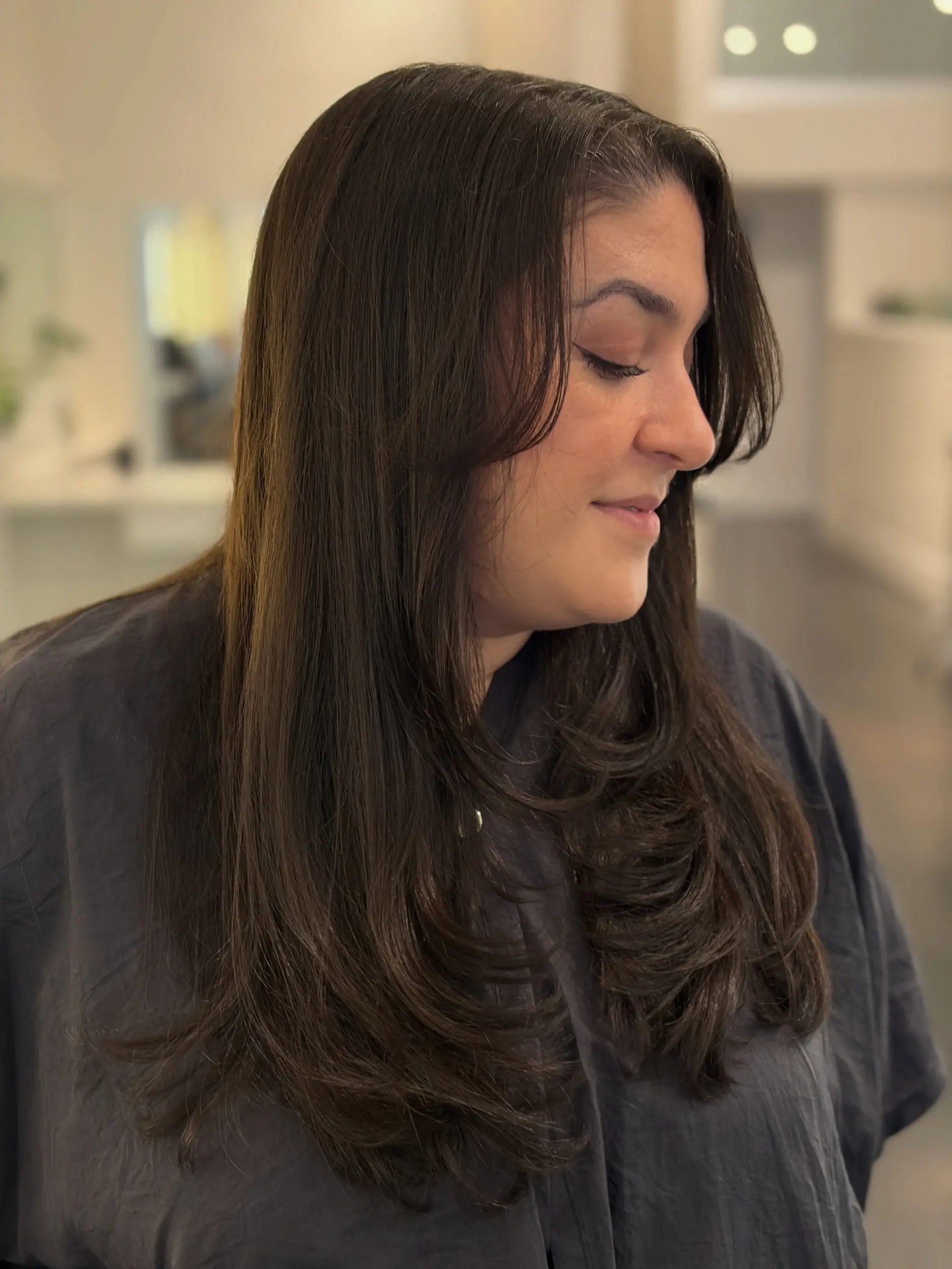 Long dark brown hair styled with smooth face-framing layers and soft curtain bangs with curled-under ends. 1