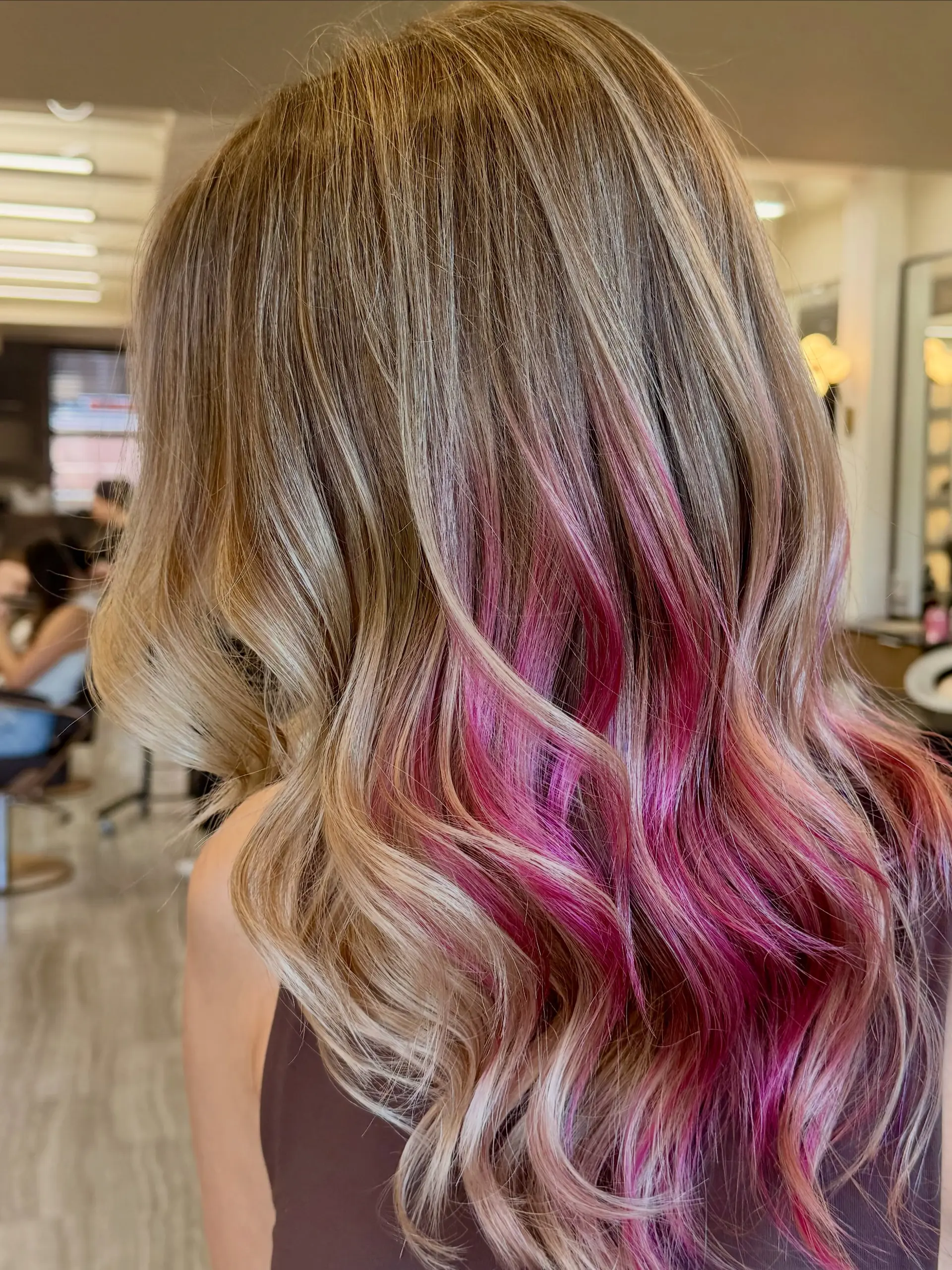 Medium-to-long dimensional blonde hair styled in soft, loose waves featuring a vivid hot pink peekaboo underlayer. 1