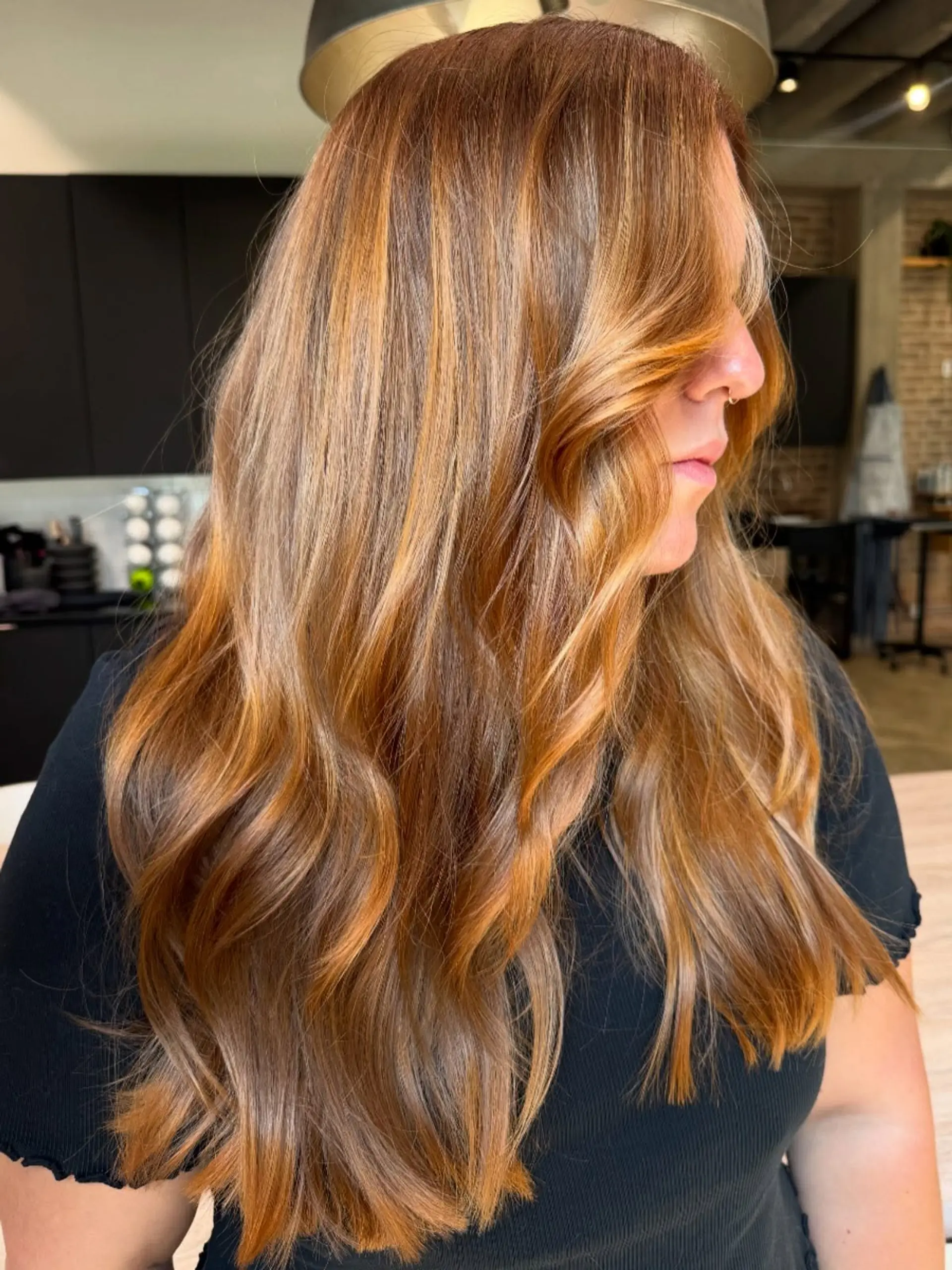 Long, flowing hair styled with soft, voluminous waves and face-framing layers, enhanced by a multi-tonal copper and golden blonde balayage for a radiant, dimensional look. 1