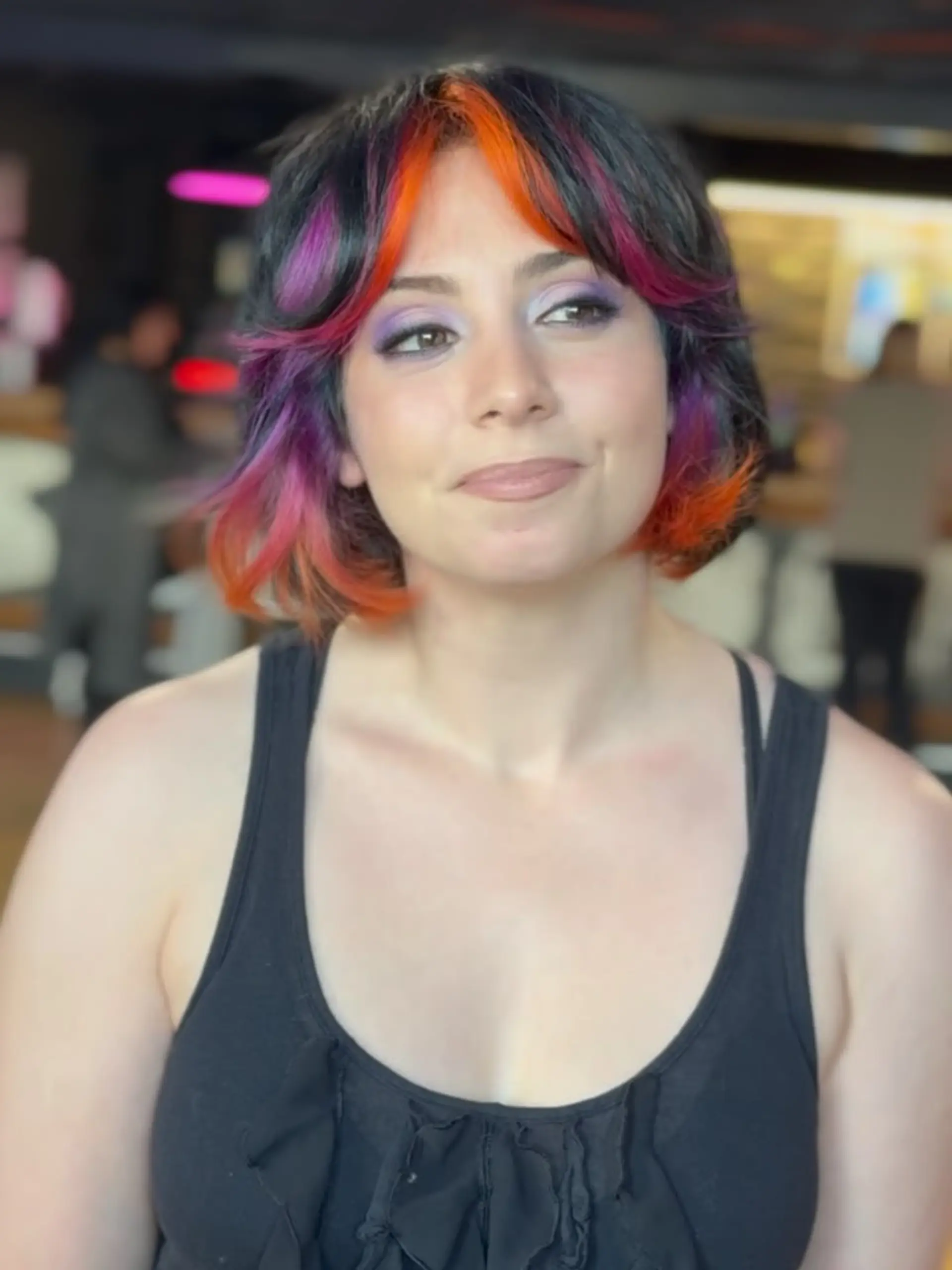 A textured short shag bob featuring curtain bangs with bright neon orange and magenta color panels over a dark base. 1