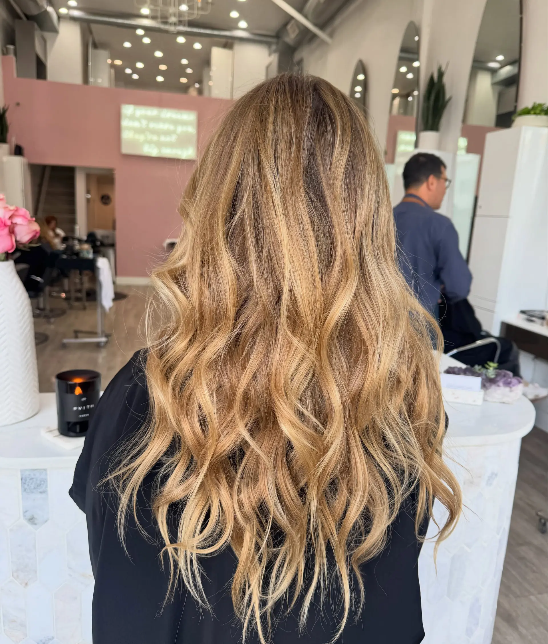 Long sun-kissed bronde hair styled with loose, dimensional beach waves flowing past the shoulders. Estimate scope: Haircut and styling only. The sun-kissed blonde/highlight color described is not priced by this mapped estimate. Published salon-level starting/range estimate; confirm the chosen provider’s quote. 1