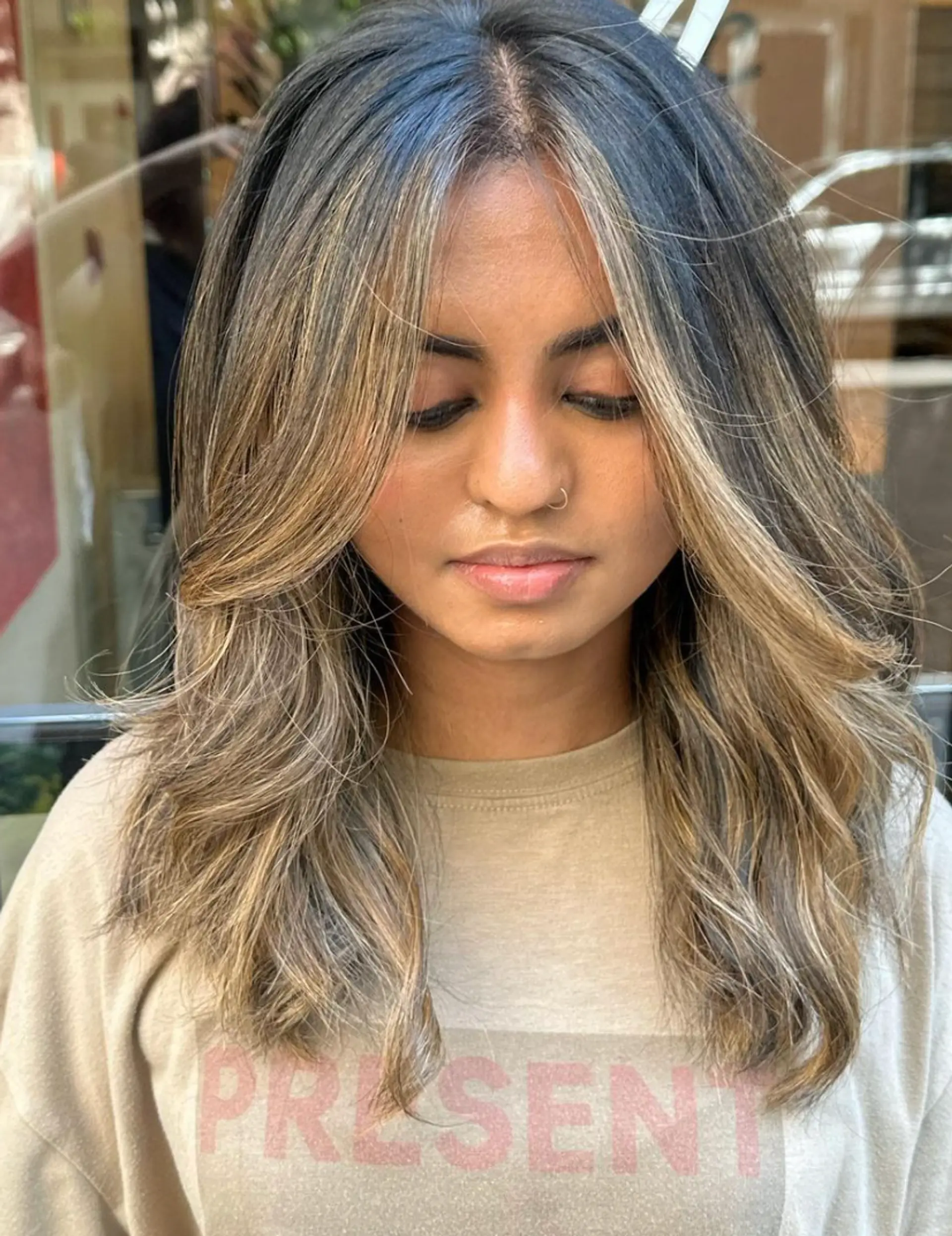 Medium-length wavy hair with a center part, layers, and blonde highlights creating a sunlit effect. The face-framing highlights and soft waves give a natural, effortless look.

Color by @simabeautynyc 1