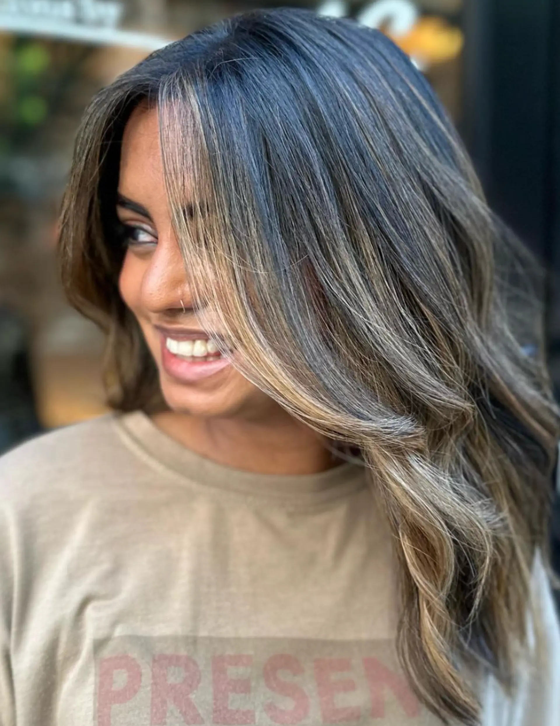 Medium-length wavy hair with a center part, layers, and blonde highlights creating a sunlit effect. The face-framing highlights and soft waves give a natural, effortless look.

Color by @simabeautynyc 2