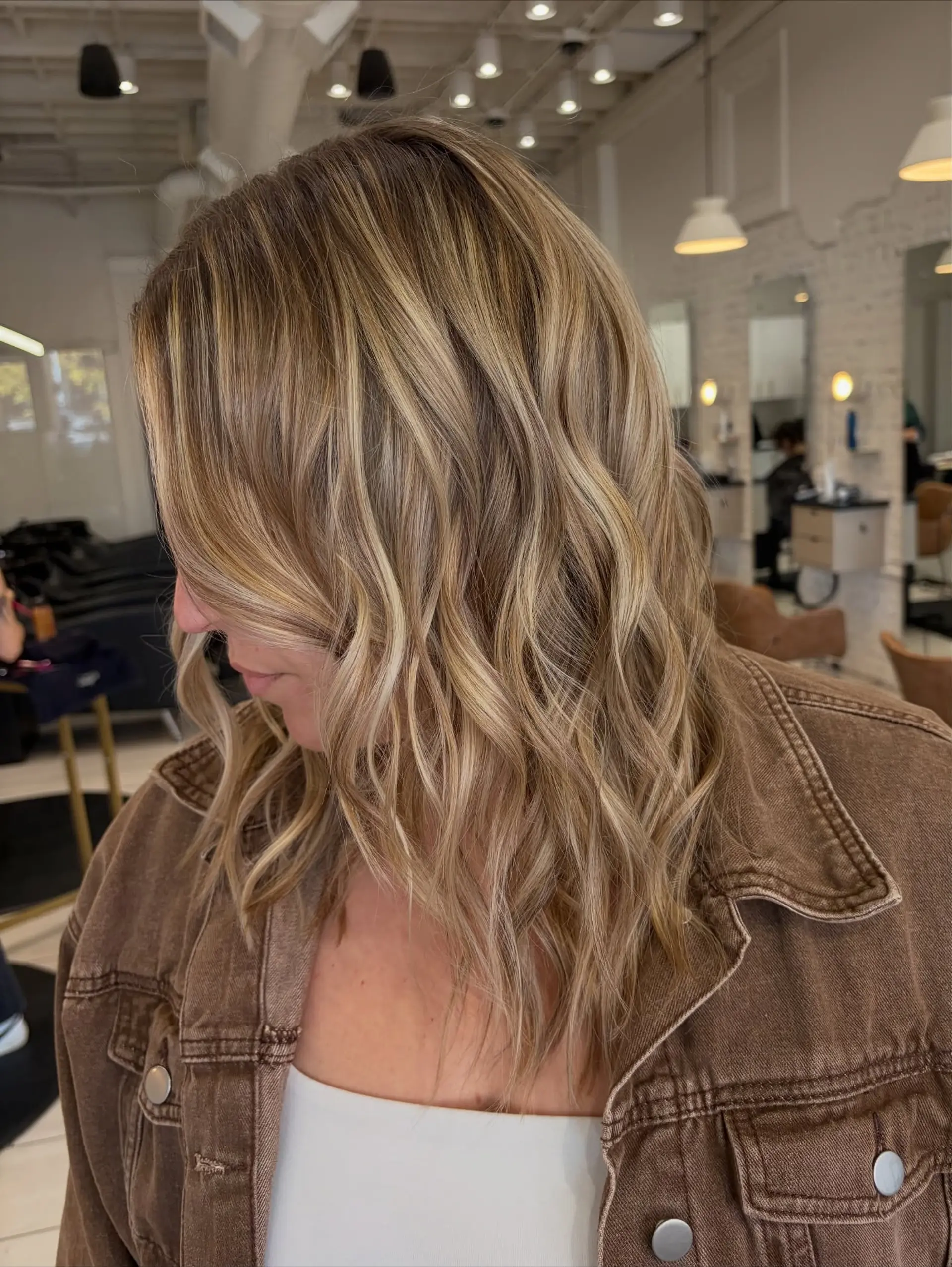 Medium-length textured cut featuring seamless, dimensional blonde balayage styled in loose waves. 1