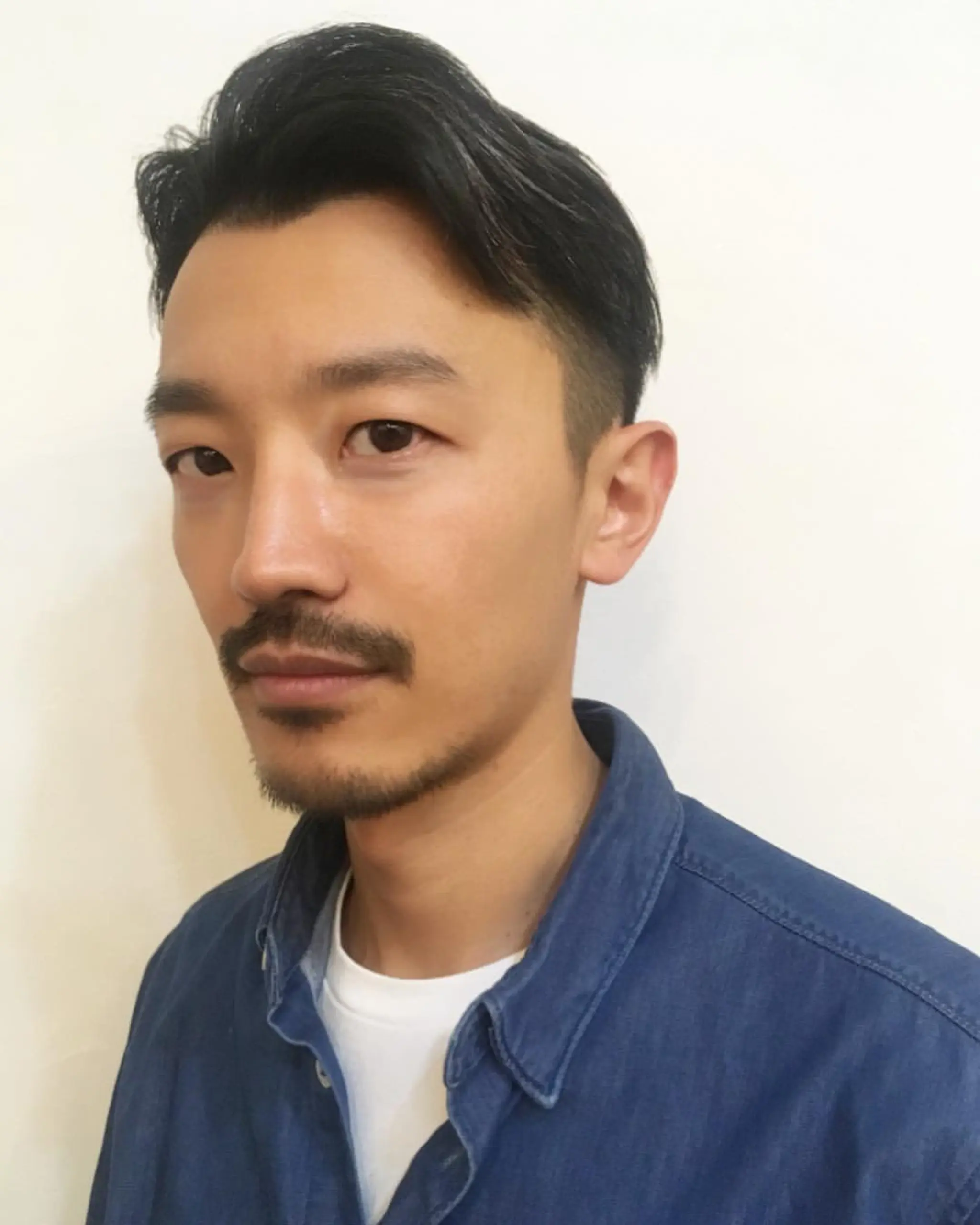 Short, straight black hair styled in a sleek side sweep with an undercut on the sides. The top is slightly longer, brushed to the side for a polished and sophisticated look.