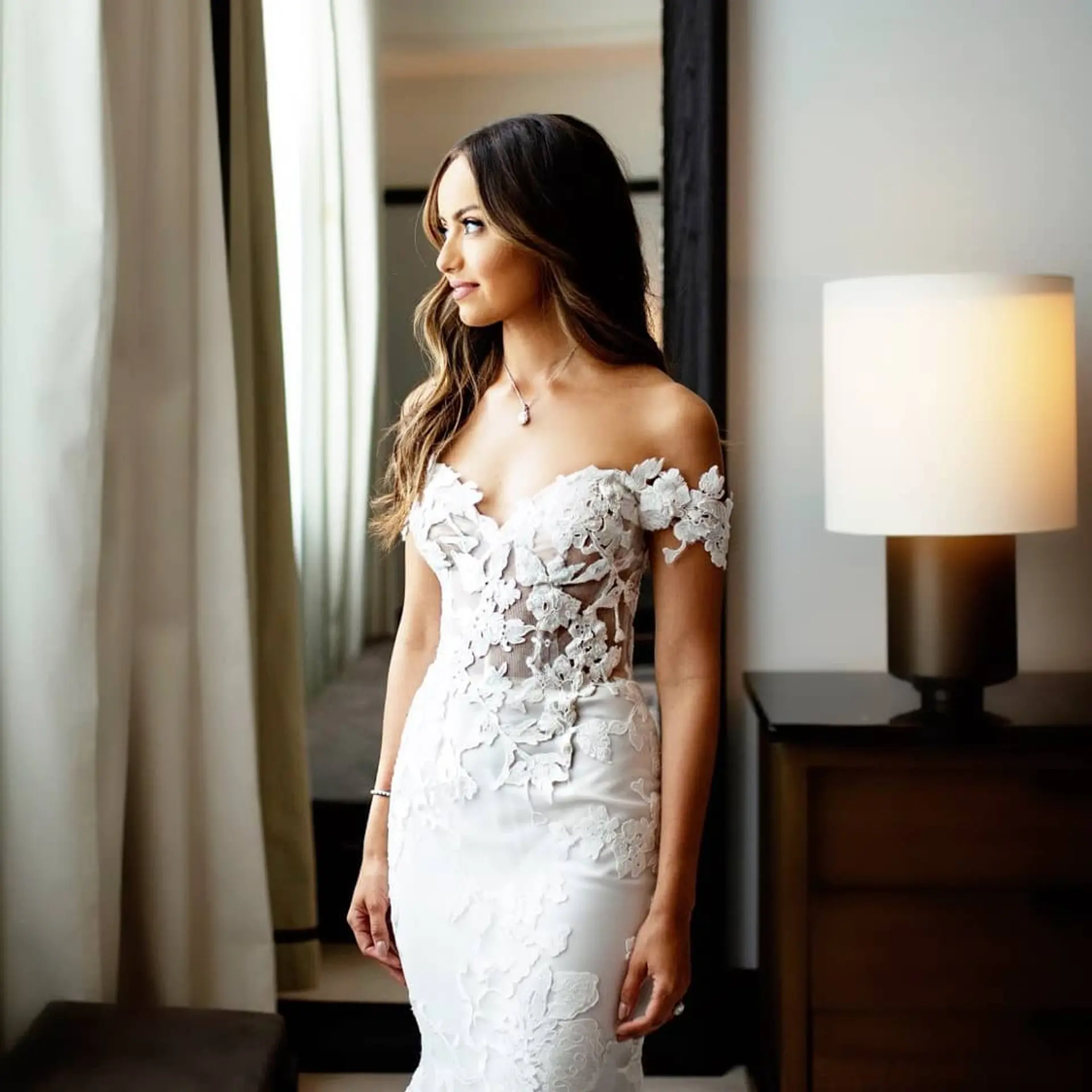 A bridal look featuring long, cascading brown hair styled in soft waves with dimensional caramel balayage and blended layers. 1