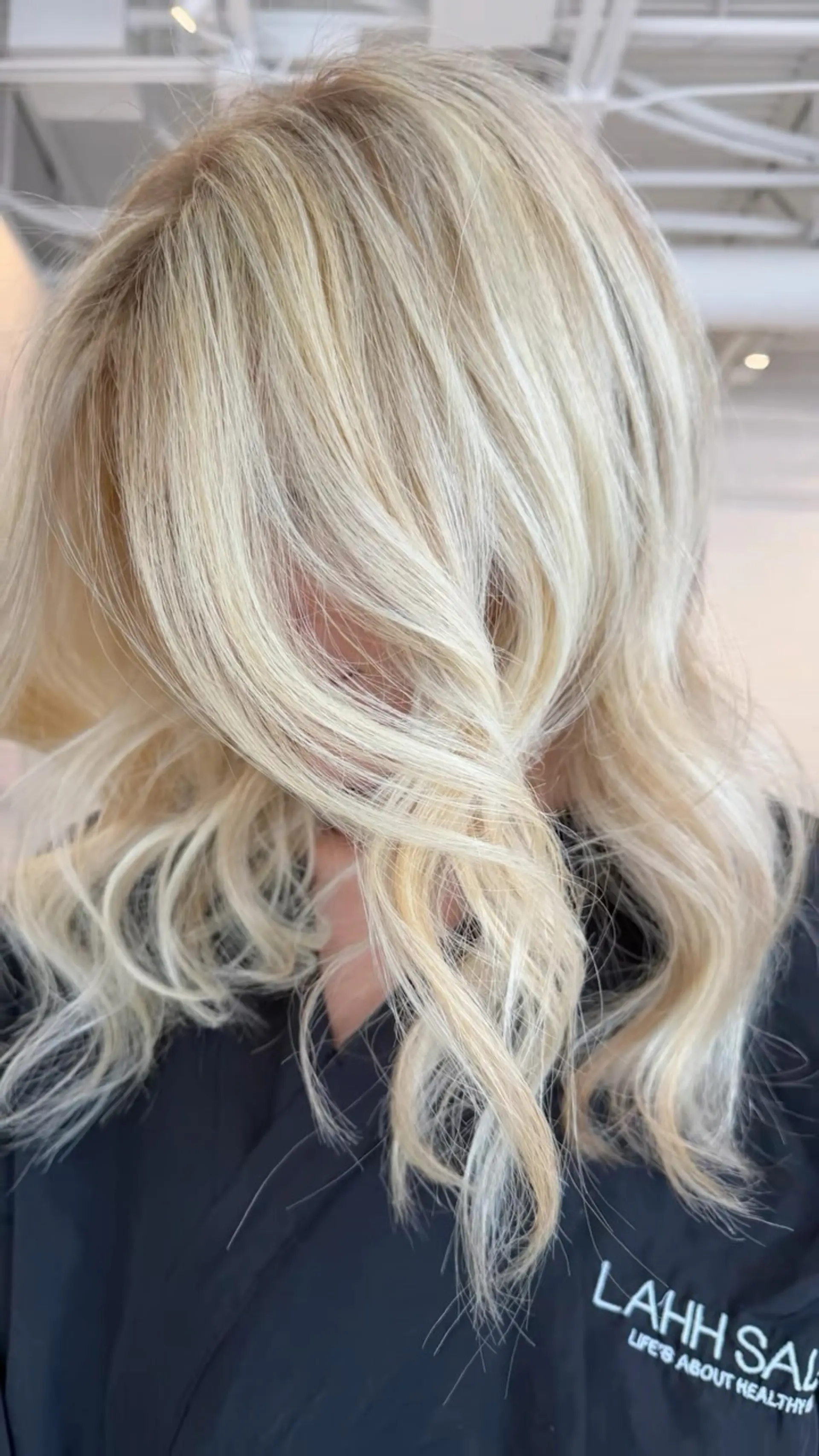 Medium-length buttery blonde hair styled in soft, loose waves framing the face. 1