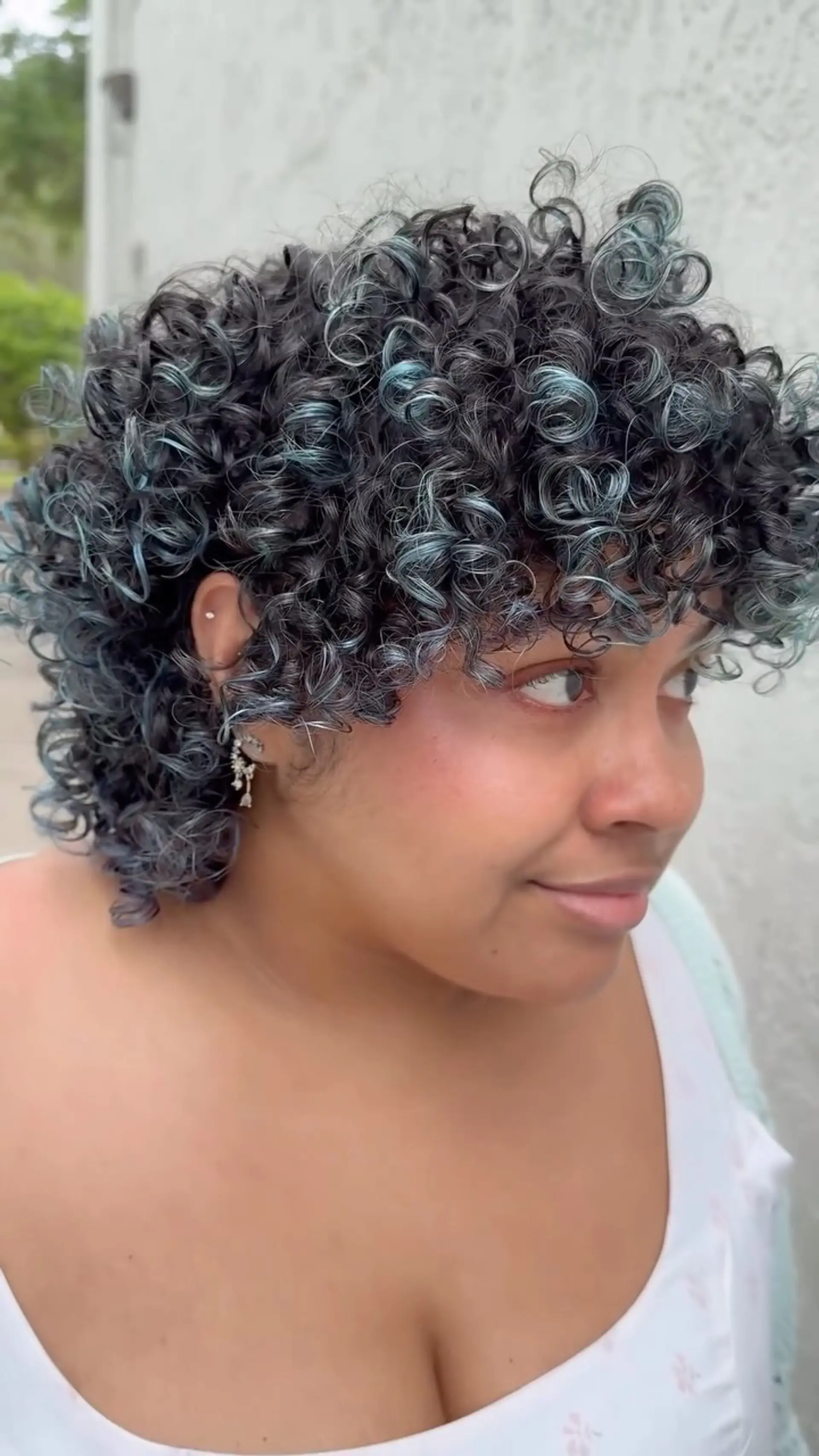 A short, voluminous curly cut featuring defined ringlets, face-framing curly bangs, and muted blue highlights. 1
