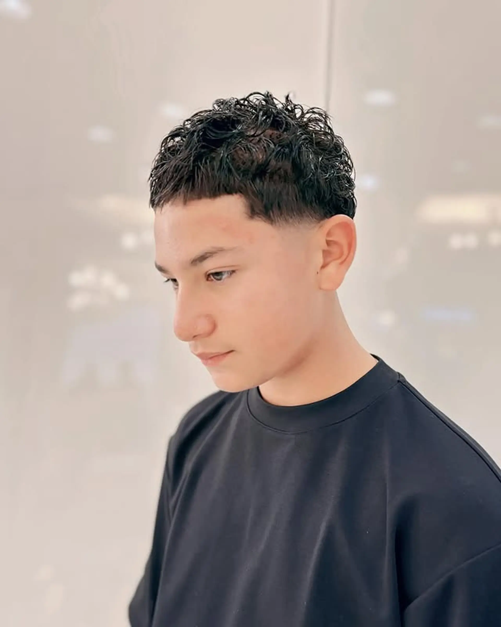 Short, tapered haircut with tight curls on top and a cropped fringe. 1