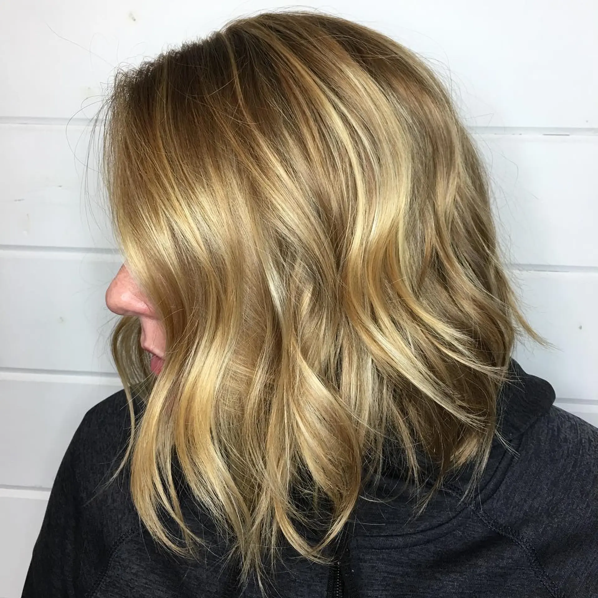 A textured shoulder-length lob styled in loose waves with multidimensional golden blonde balayage. 1