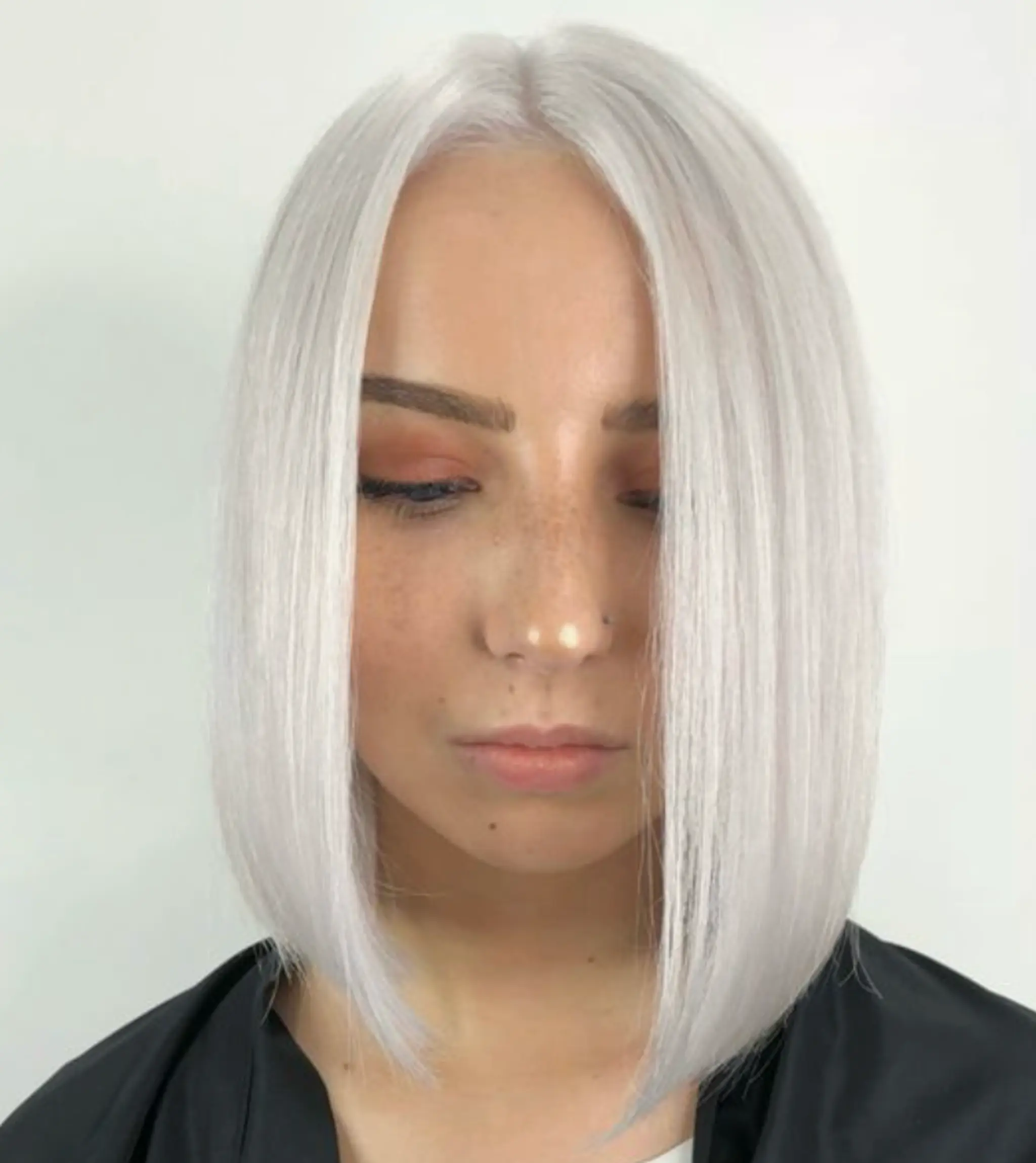 Striking medium-length blunt bob with platinum blonde hair, impeccably straight and smooth, featuring a center part.