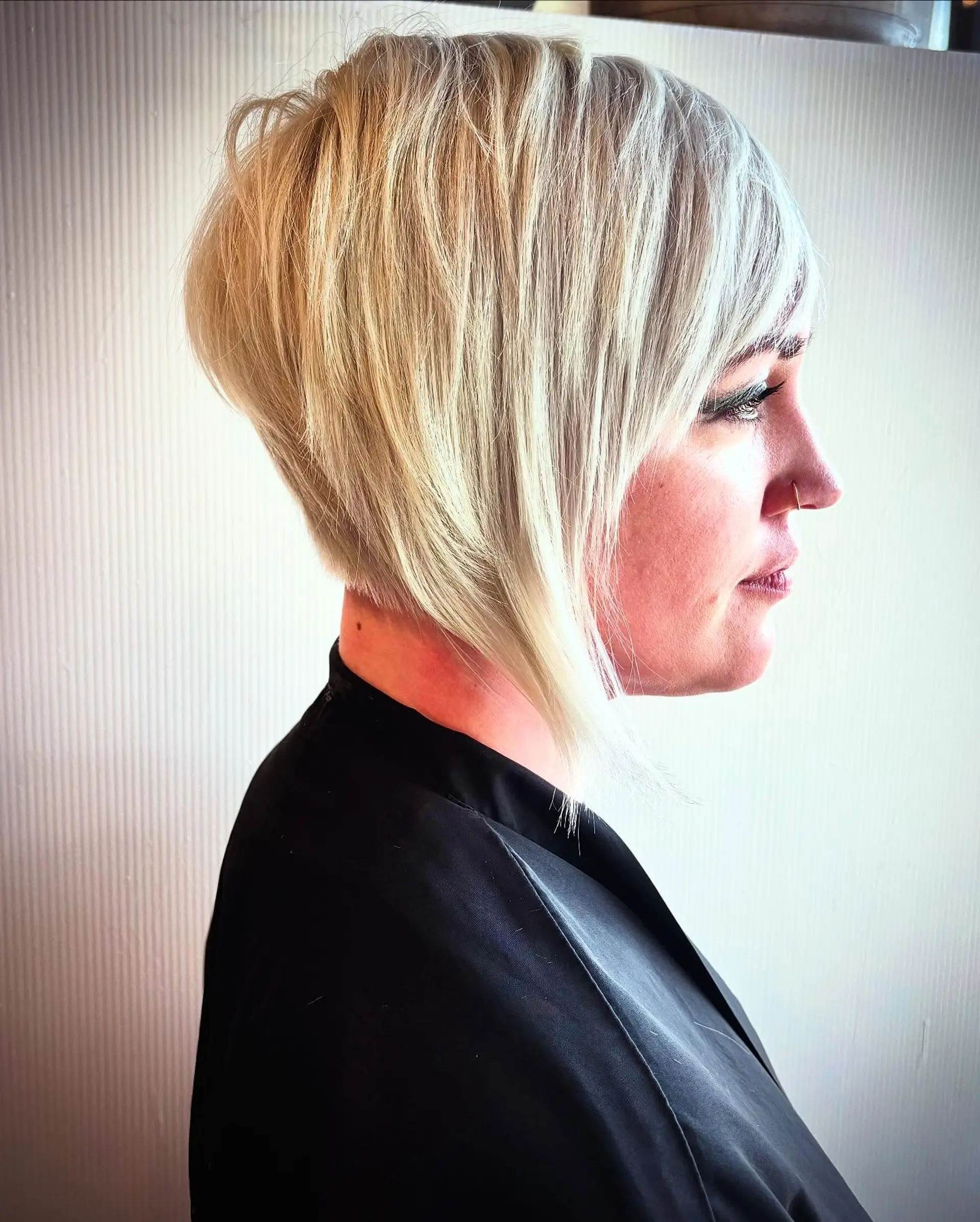 A sharply angled, textured inverted bob featuring stacked volume at the nape and side-swept fringe in a platinum blonde hue. 1