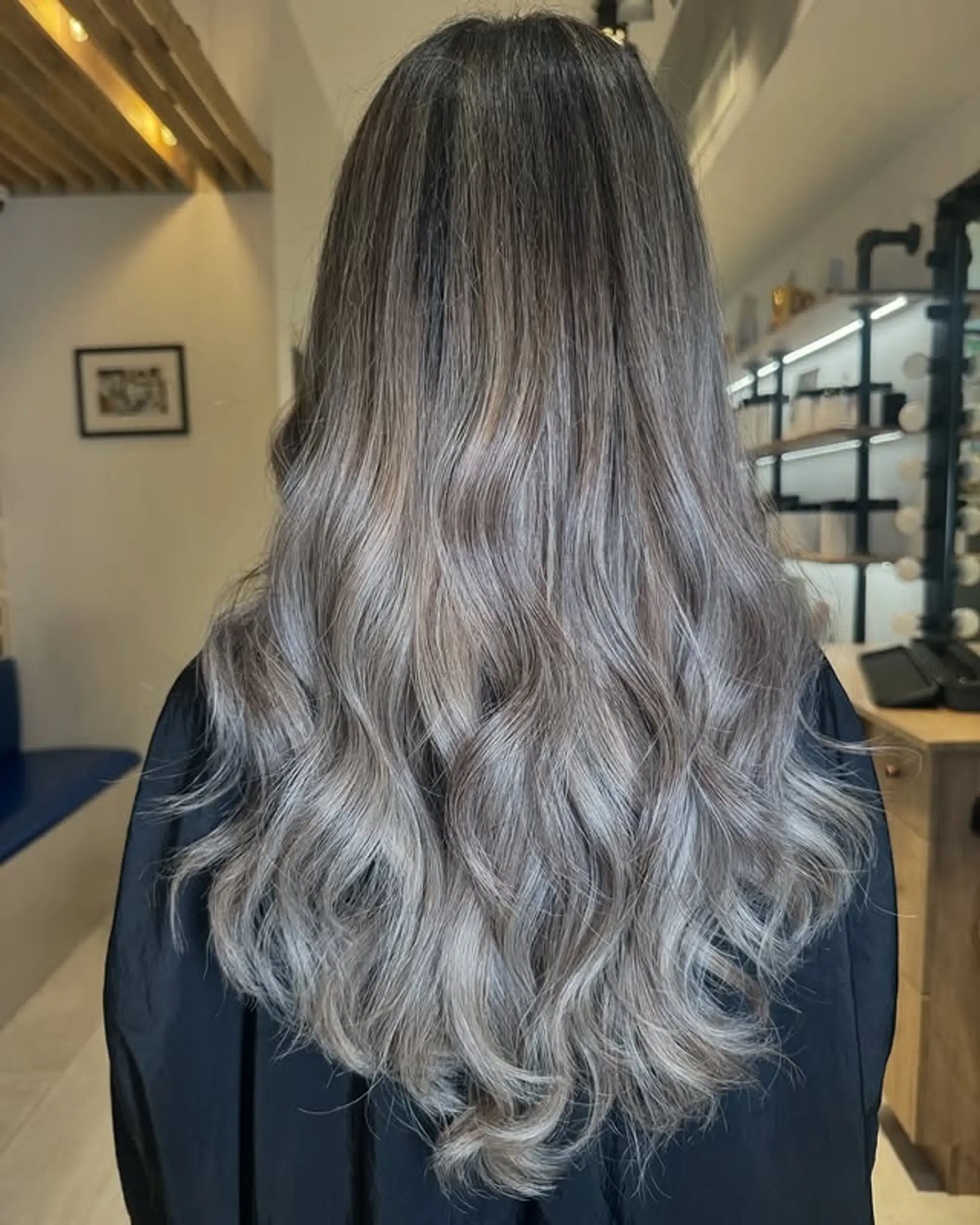 Long wavy hair with a smoky ash balayage, transitioning from darker roots to cool silver-gray ends. 1