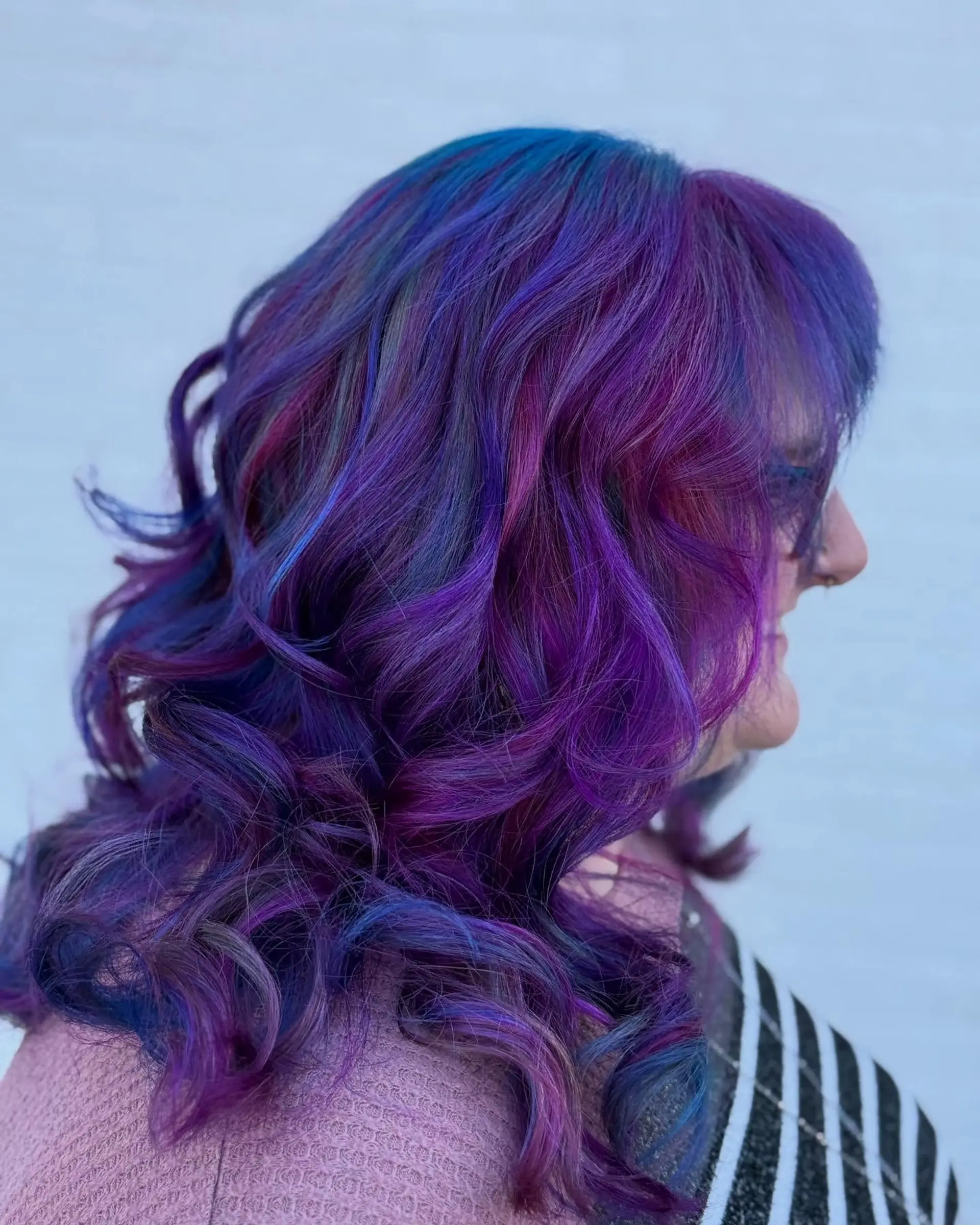 Medium-length layered hair styled in bouncy, loose curls featuring a vivid multi-tonal blend of deep purple, vibrant magenta, and rich blue tones. 1