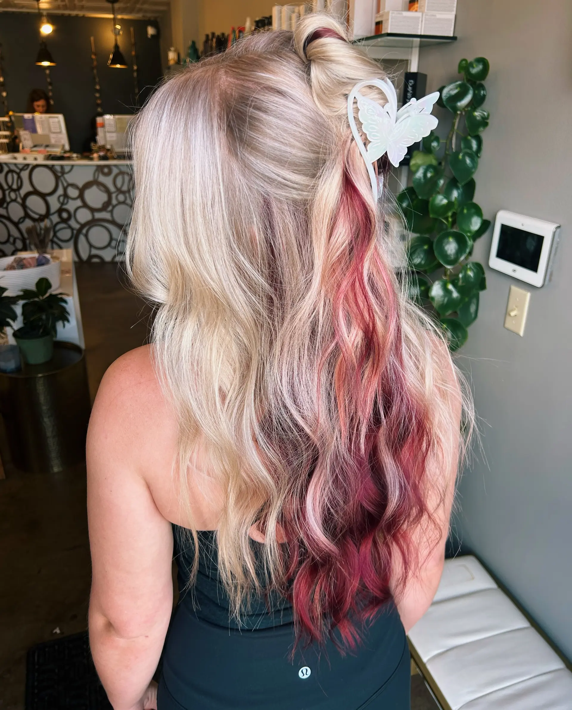 Long platinum blonde hair featuring a vibrant magenta peekaboo underlayer, styled in a half-up twist with an iridescent butterfly claw clip. 1