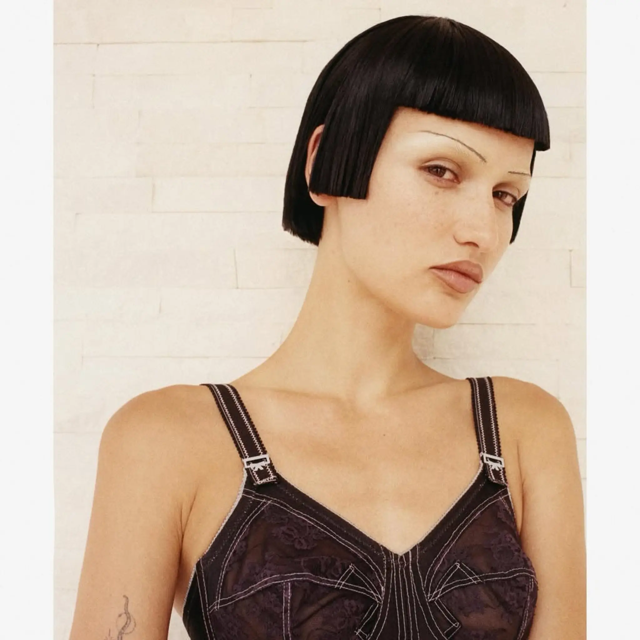 A sleek, short bob with jet black, straight hair. The cut features a blunt fringe and symmetrical, jaw-length edges with a glossy finish, influenced by retro styles.