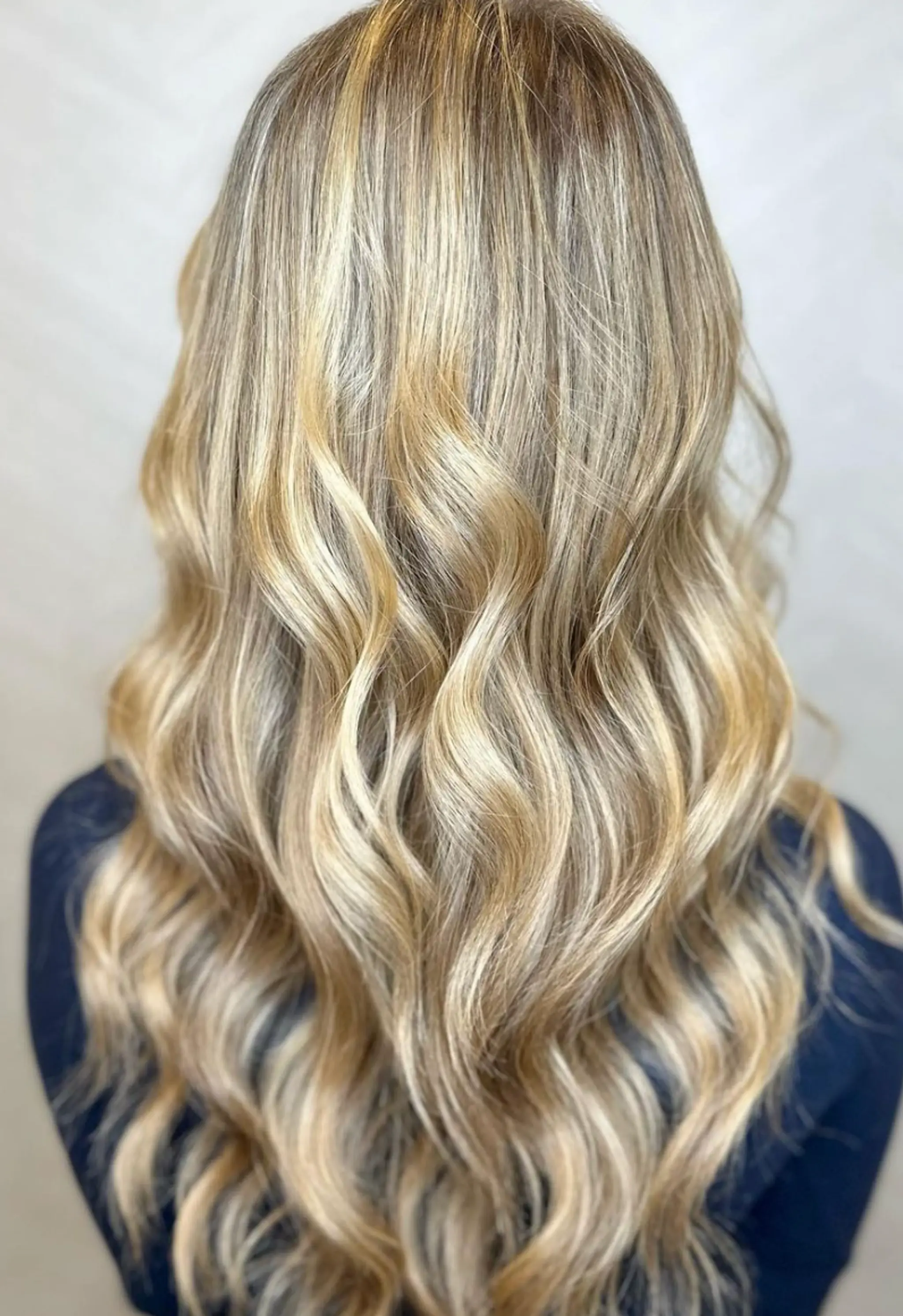 Very long, wavy blonde hair with golden and honey balayage highlights, featuring loose, glossy waves that cascade down the back.