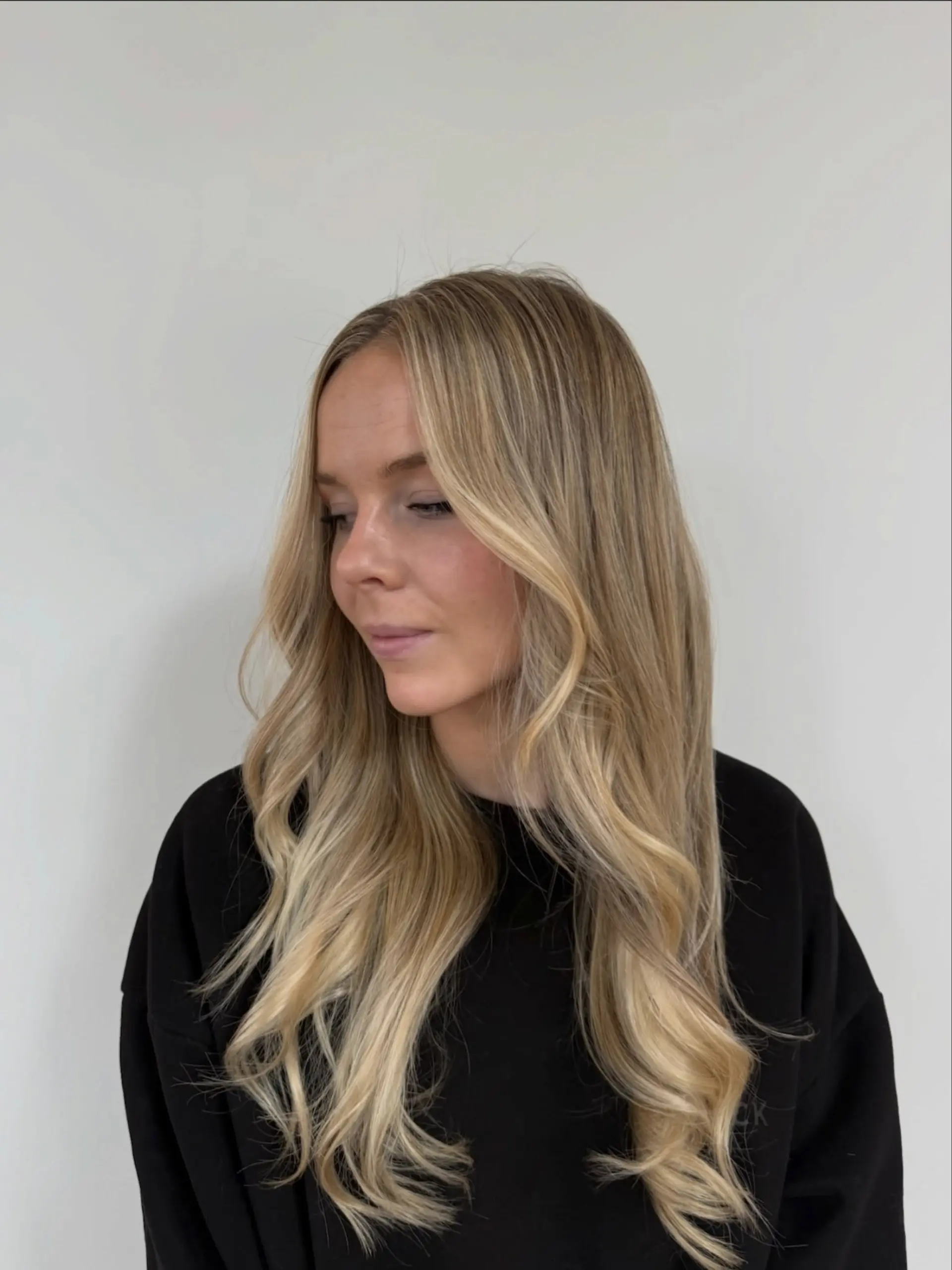 Long, multi-tonal lived-in blonde hair styled in effortless, loose waves with face-framing brightness. 1