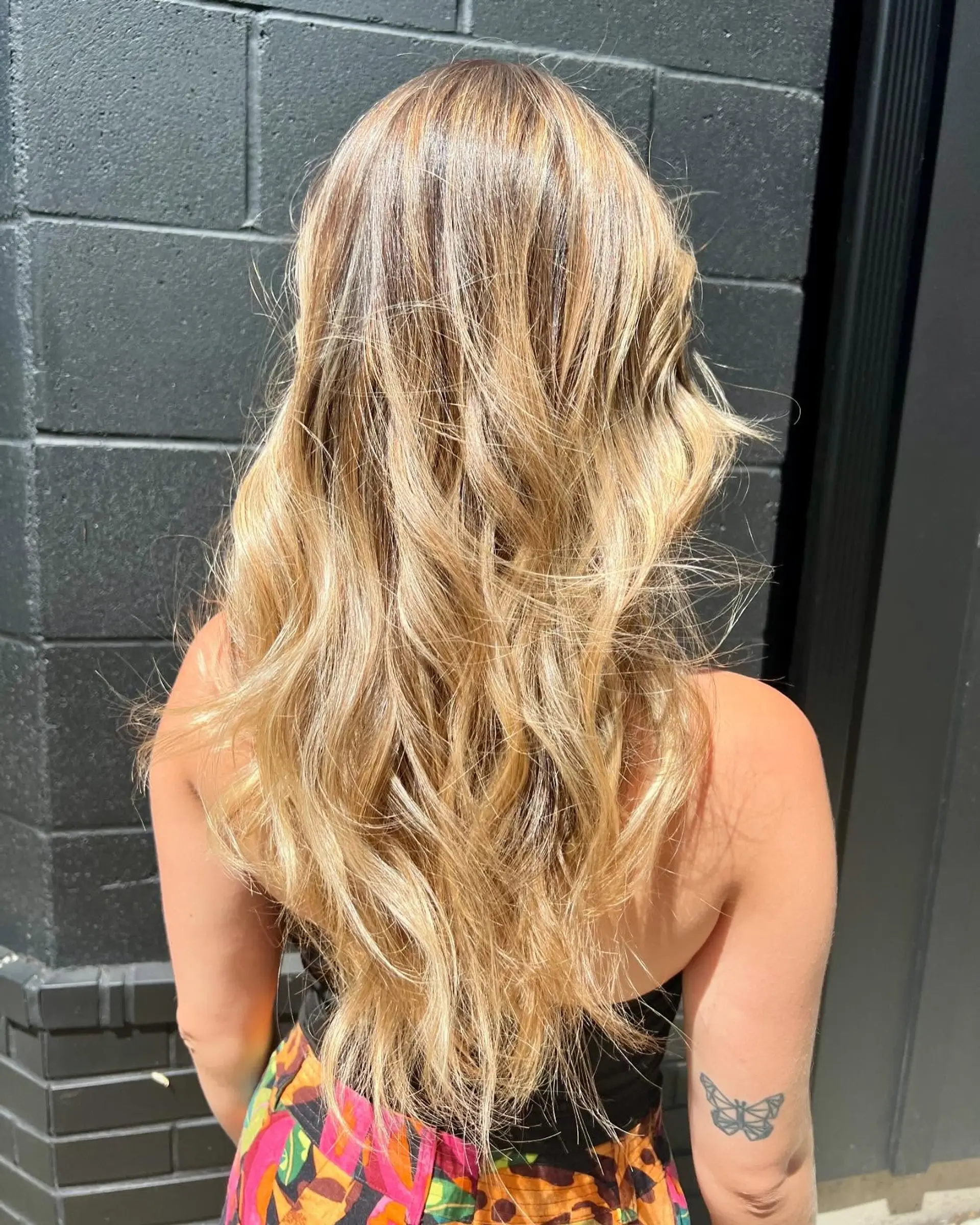 Long warm blonde hair featuring dimensional balayage styled with relaxed, textured waves. 1