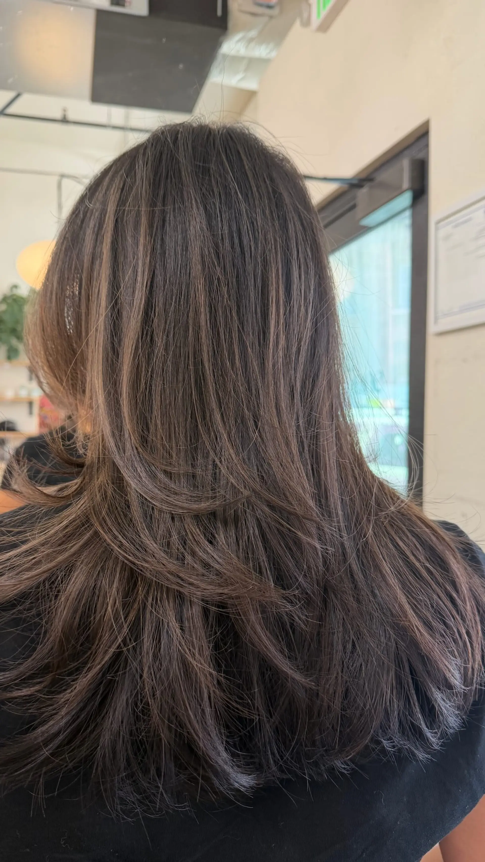 Long brunette hair styled with flowing, curved layers and subtle ash brown balayage highlights for soft dimension. 1