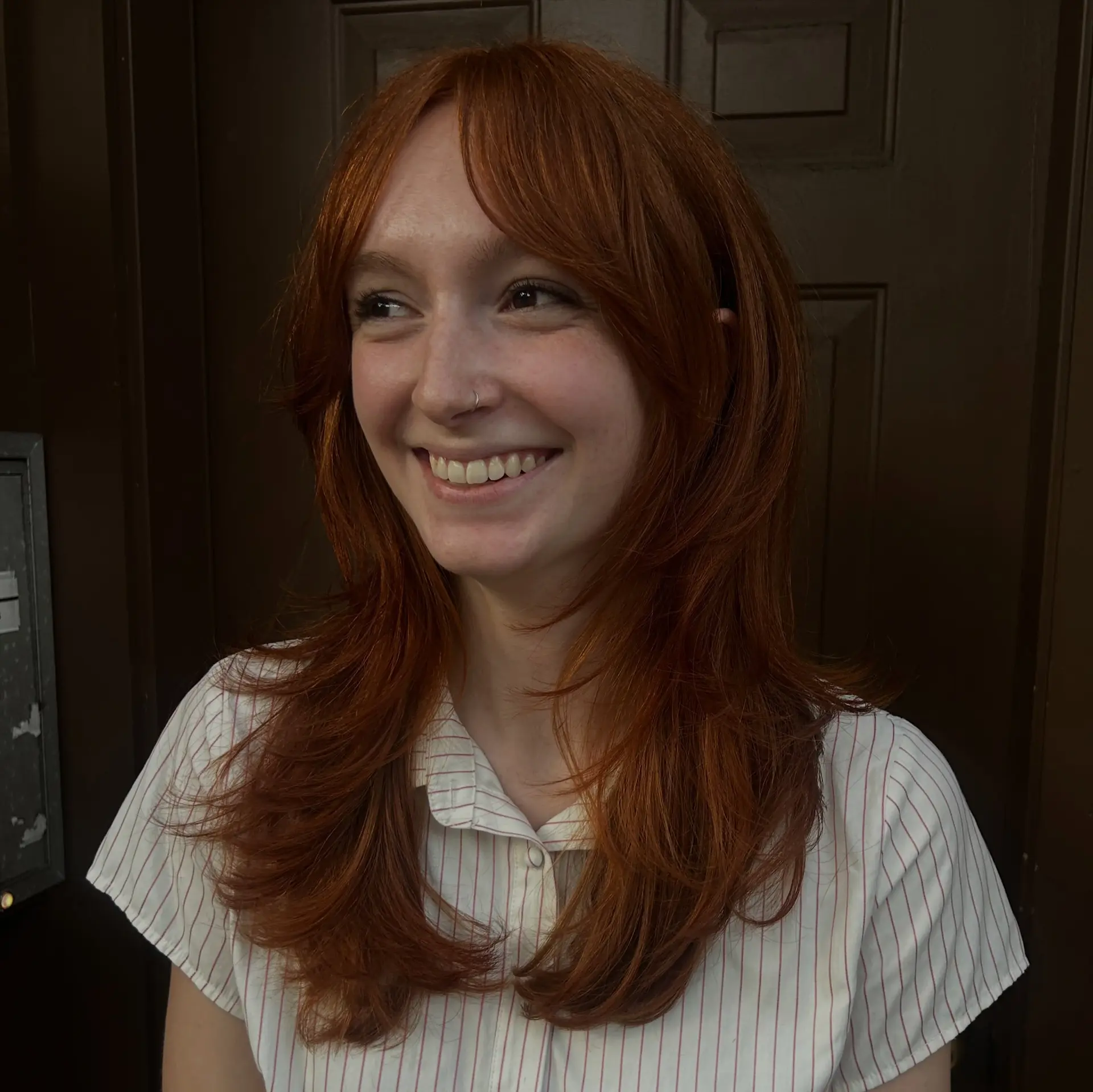 Vibrant copper layered haircut featuring face-framing layers, soft curtain bangs, and feathered ends styled in a voluminous blowout. 1