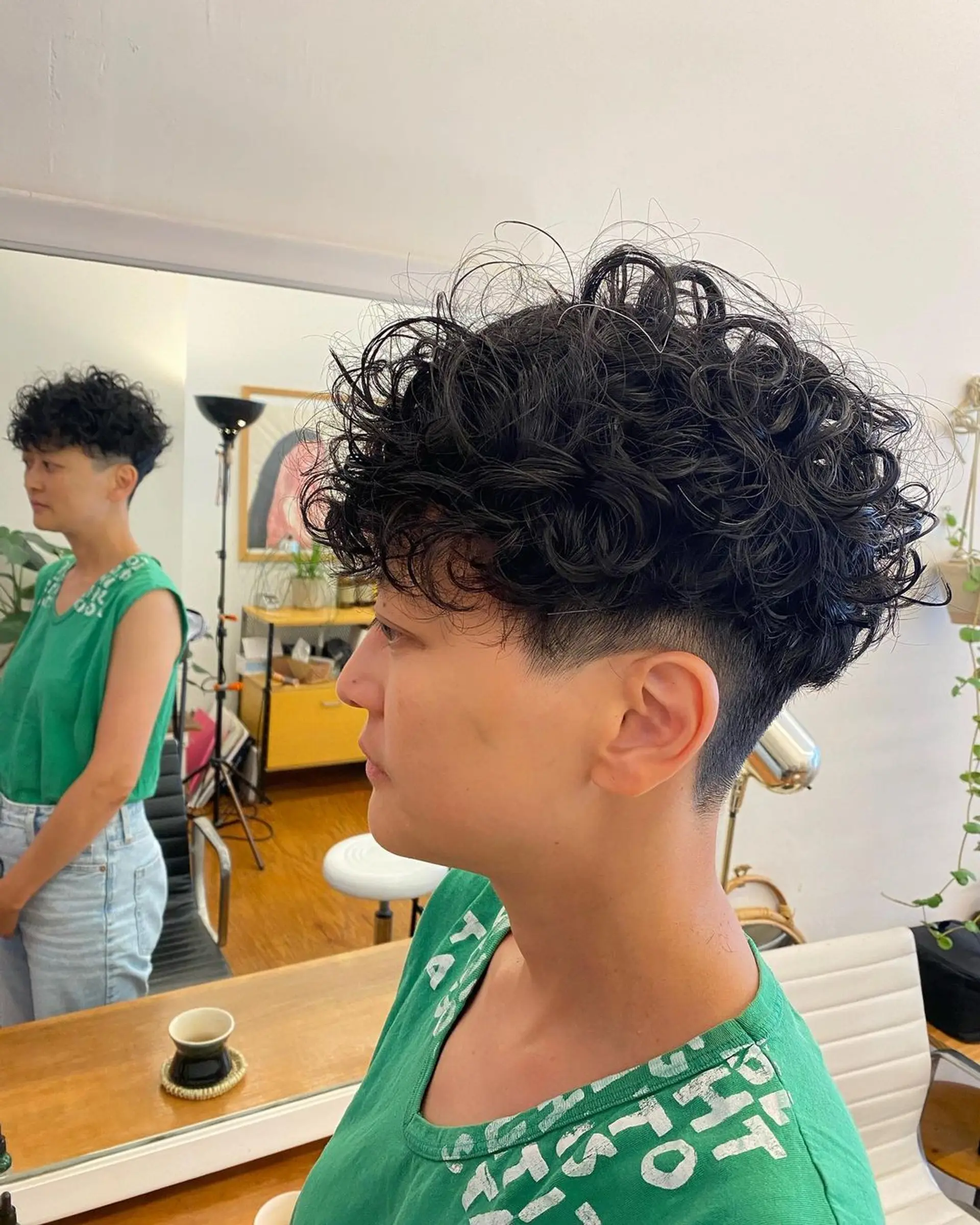 Short length with a prominent curly top, close undercut, and neatly tapered sides. The crown is voluminous and textured with black curly hair. 1
