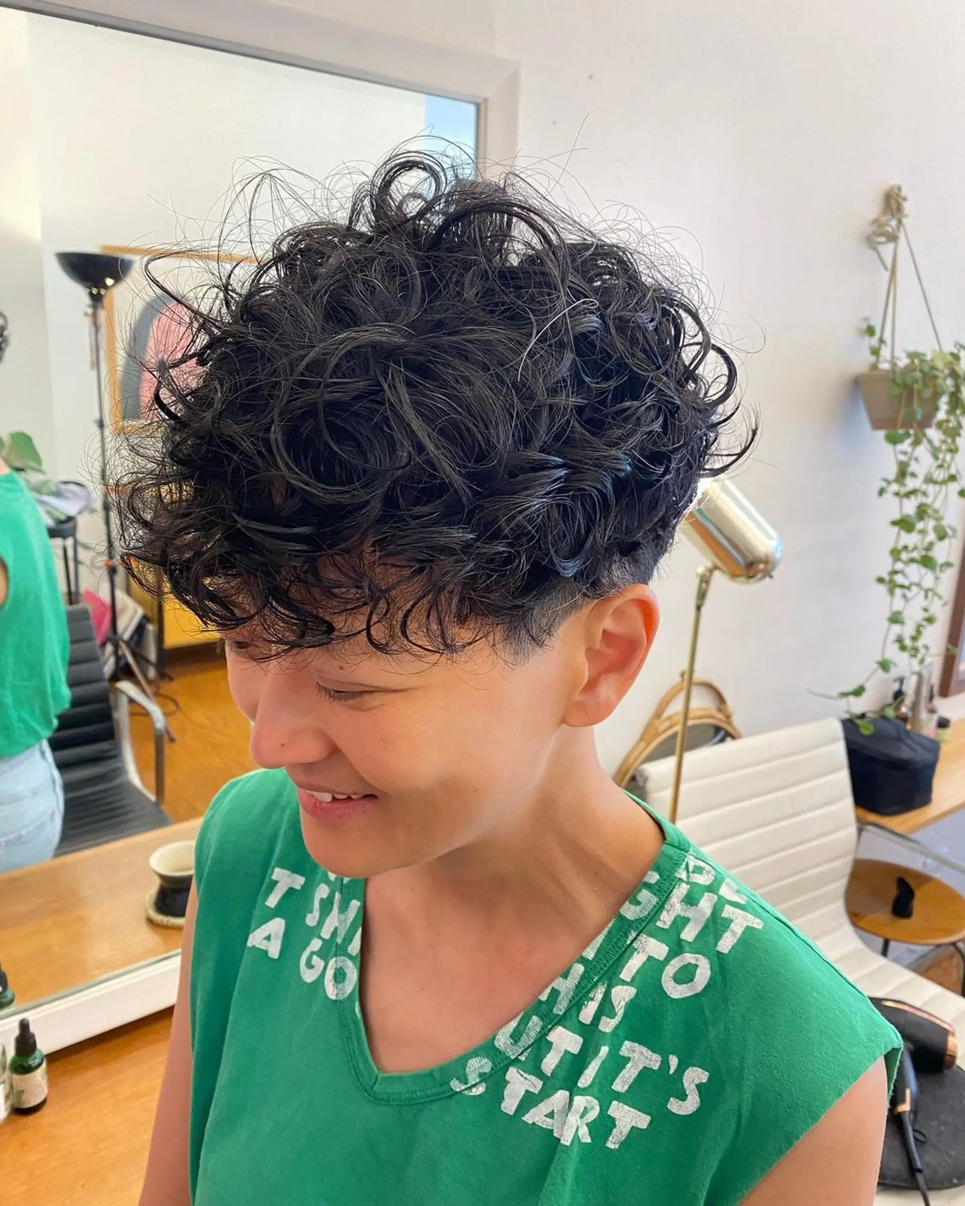 Short length with a prominent curly top, close undercut, and neatly tapered sides. The crown is voluminous and textured with black curly hair. 2