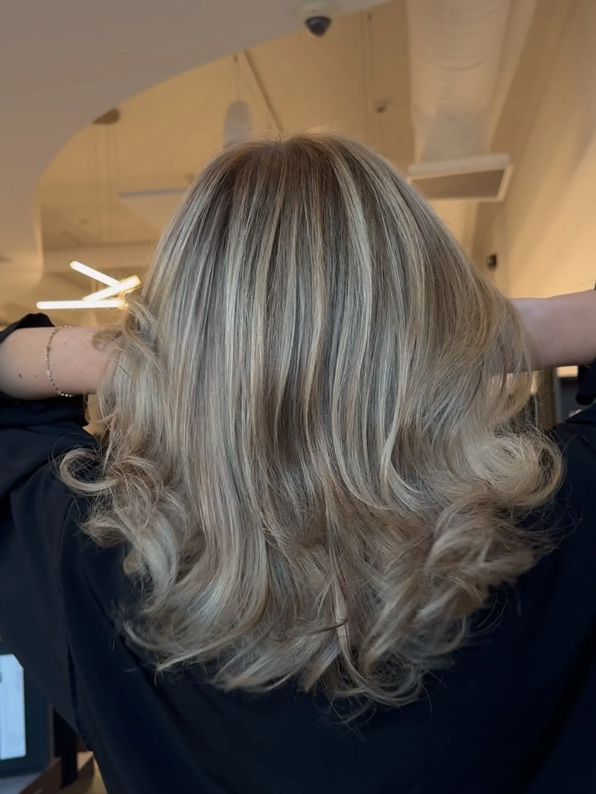 Medium-length dimensional blonde hair featuring seamless foil highlights blended over a natural light brown base, styled with soft outward curls at the ends. 1